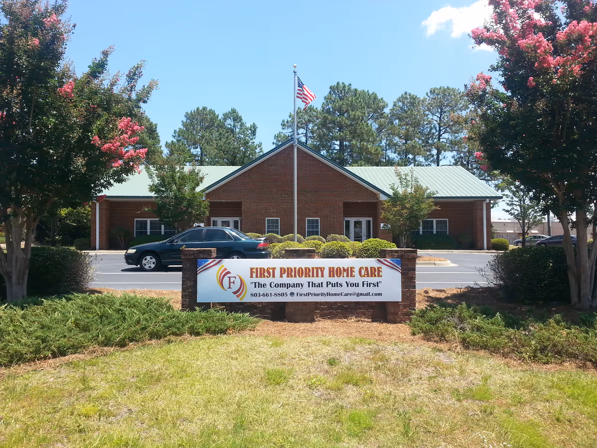 Brick building with flagpole, trimmed shrubs, and a First Priority Home Care sign.