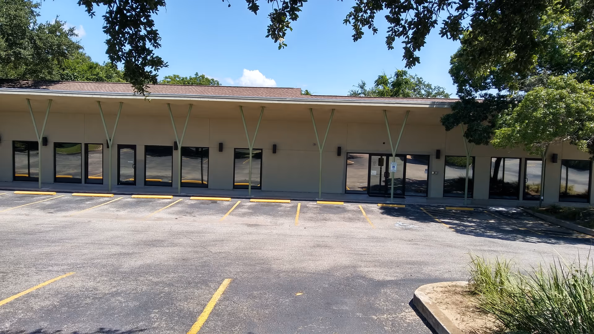 Single-story building with large glass doors and an empty parking lot in front.