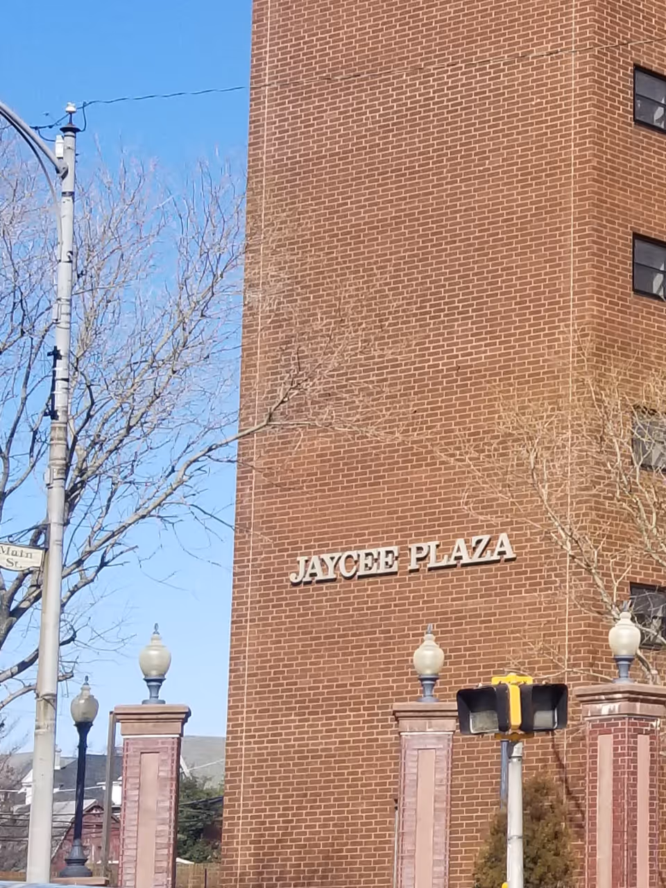 Brick building with 'JAYCEE PLAZA' sign, street lamps, and leafless trees in foreground.
