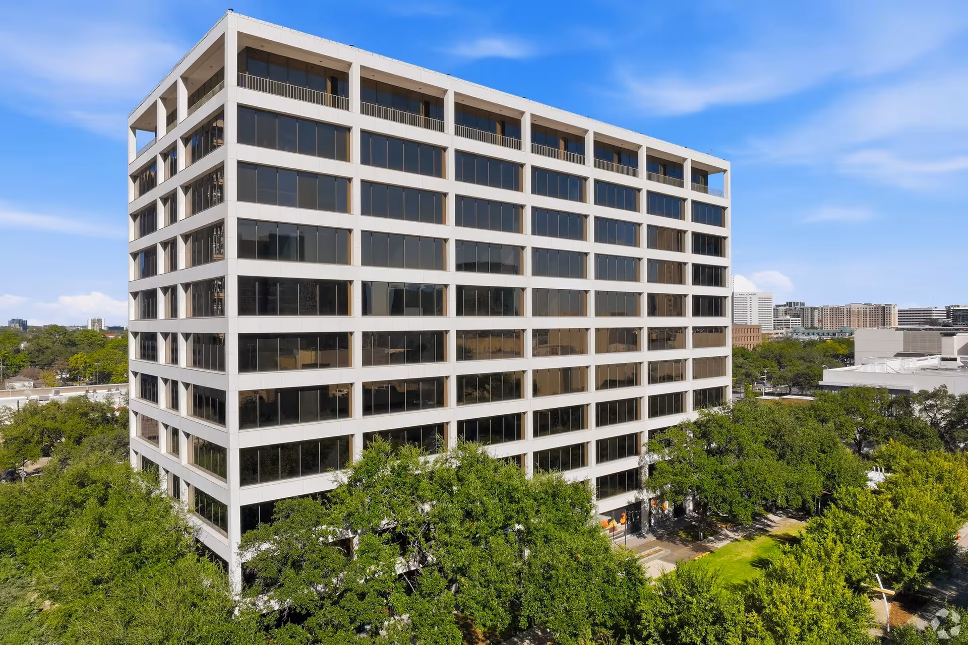 A tall modern glass and concrete building surrounded by green trees under blue sky
