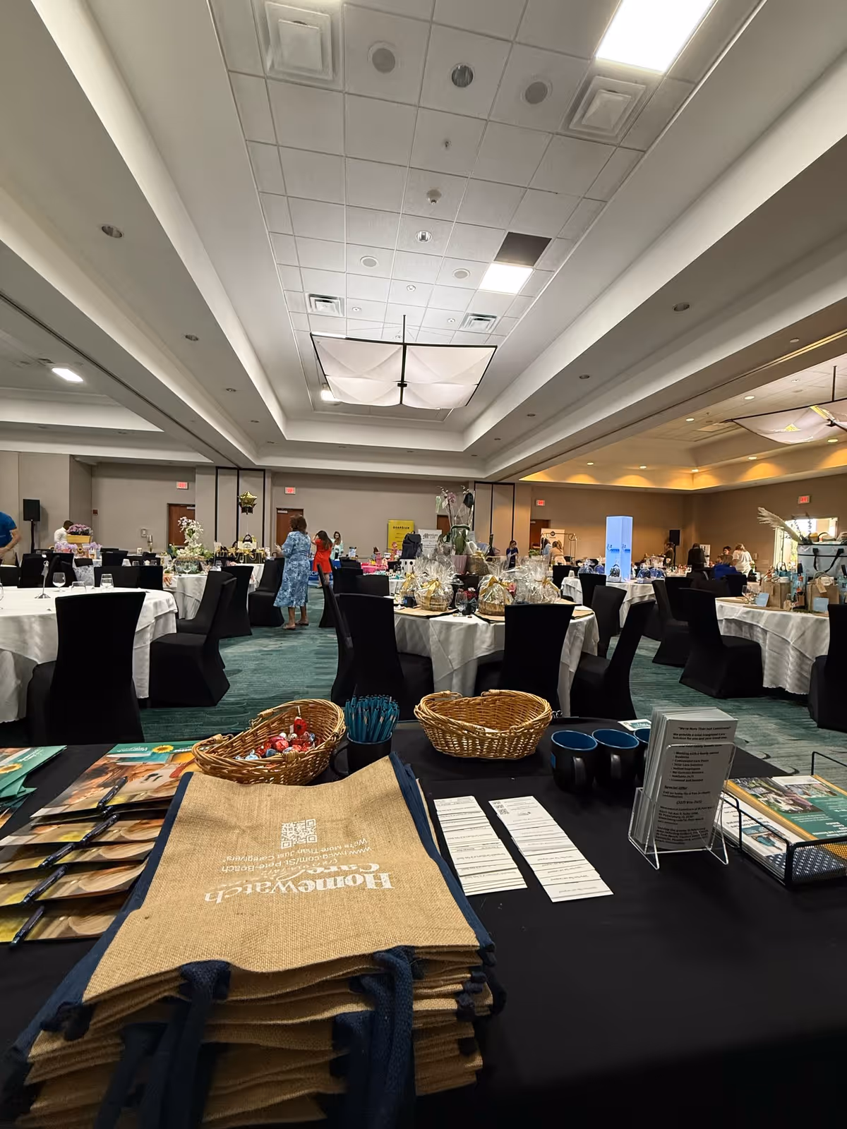Indoor dining hall with round tables, white cloths, and black chairs.