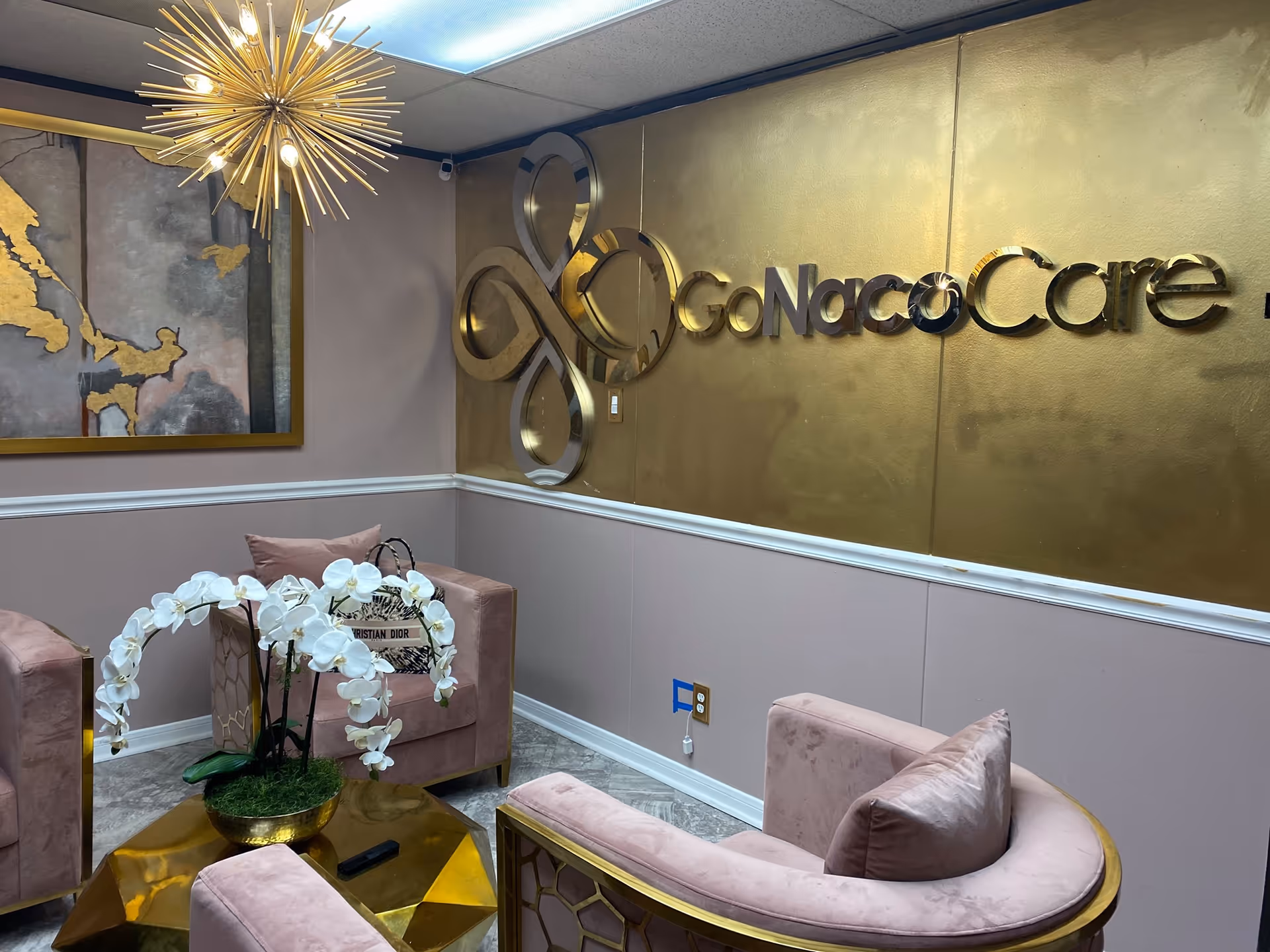 Luxurious pink seating area in a Go Naco Care lobby with a gold wall and sign.