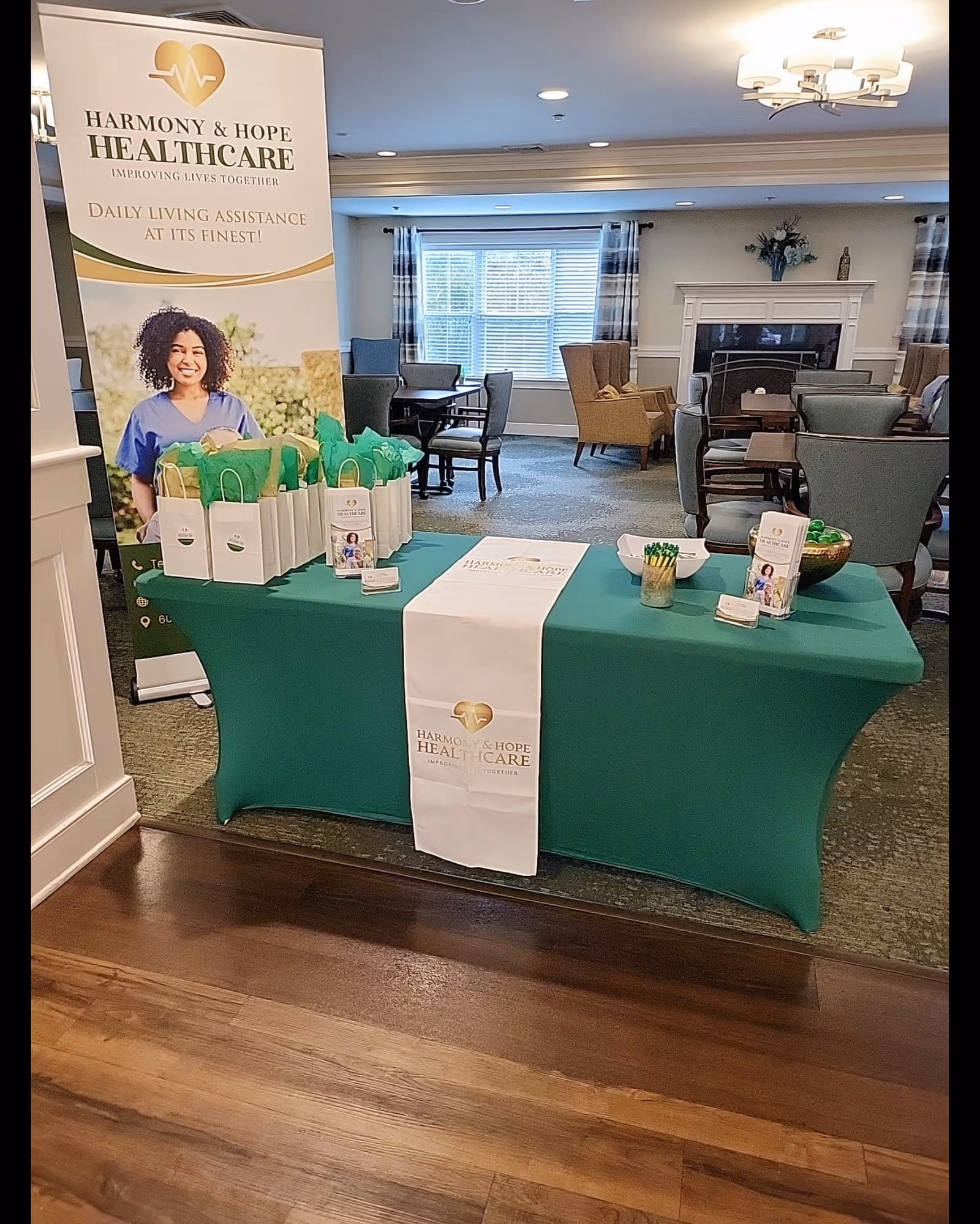 Promotional banner and green-clothed table with gift bags in a senior living lounge.