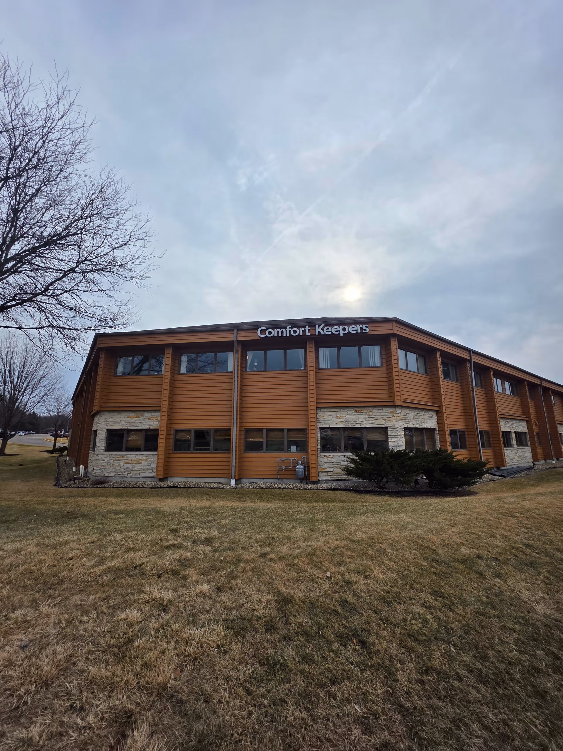 Two-story Comfort Keepers building with wood siding and stone accents on a grassy lawn.