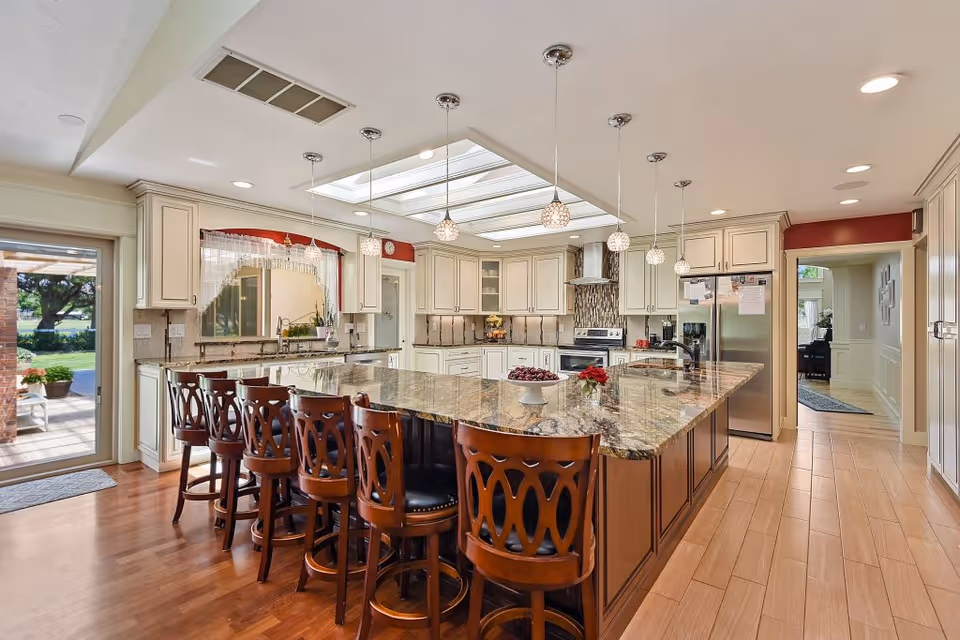 Spacious kitchen with granite island, pendant lights, and wooden seating in a senior home