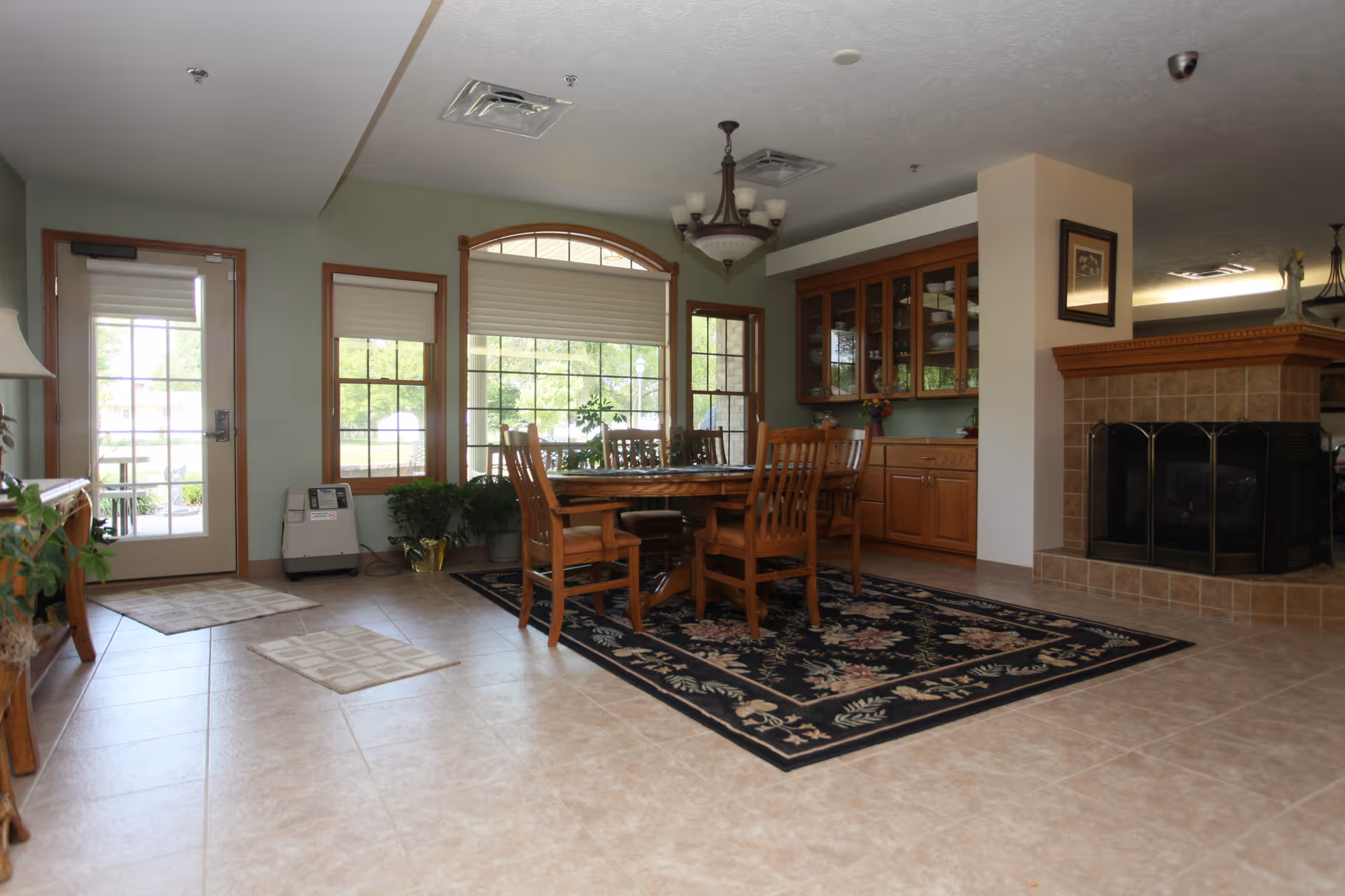 A spacious dining area with a wooden table, chairs, cabinets, windows, and a fireplace.