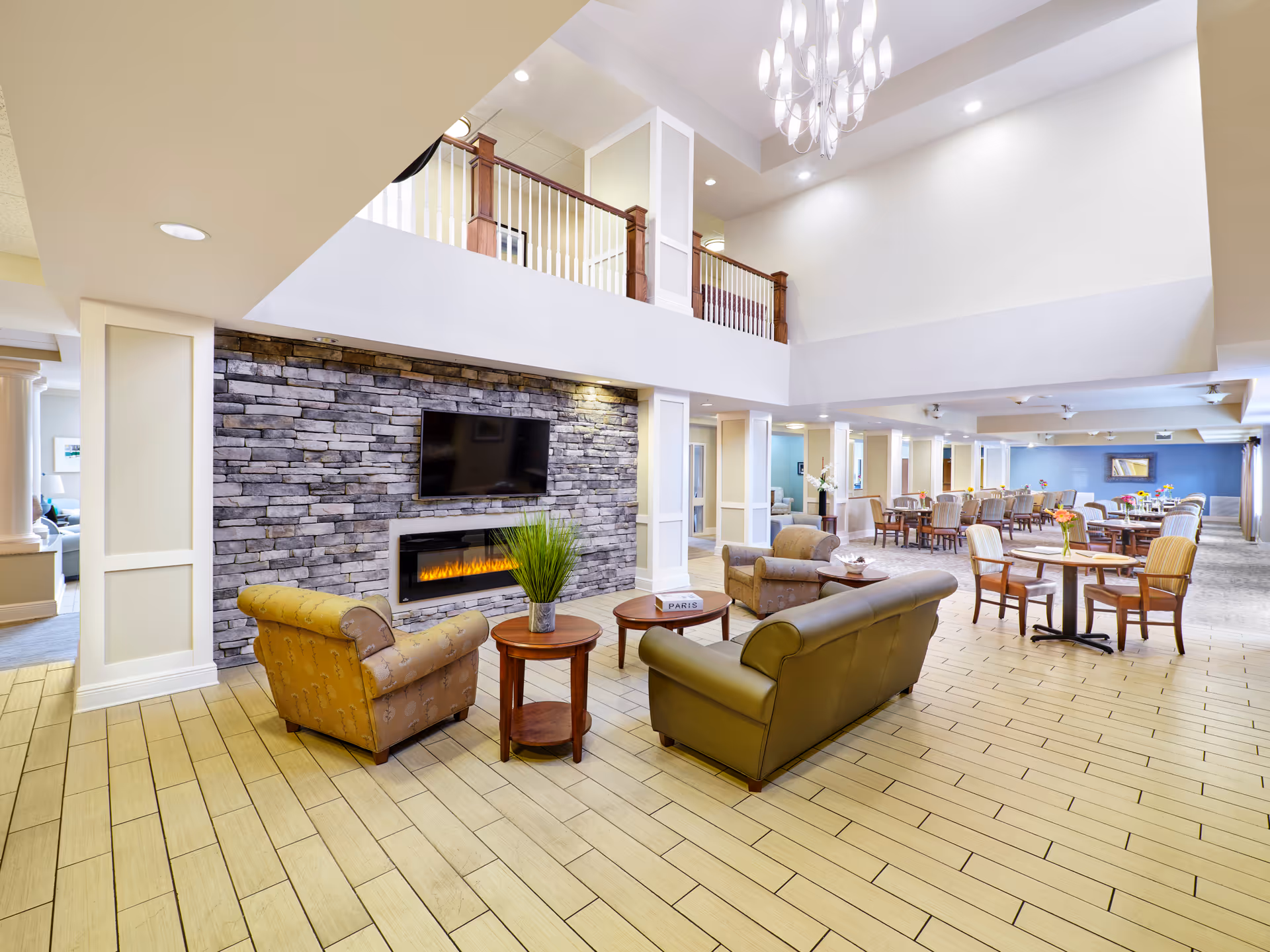 Spacious senior living lounge with stone fireplace, mounted TV, and seating area.