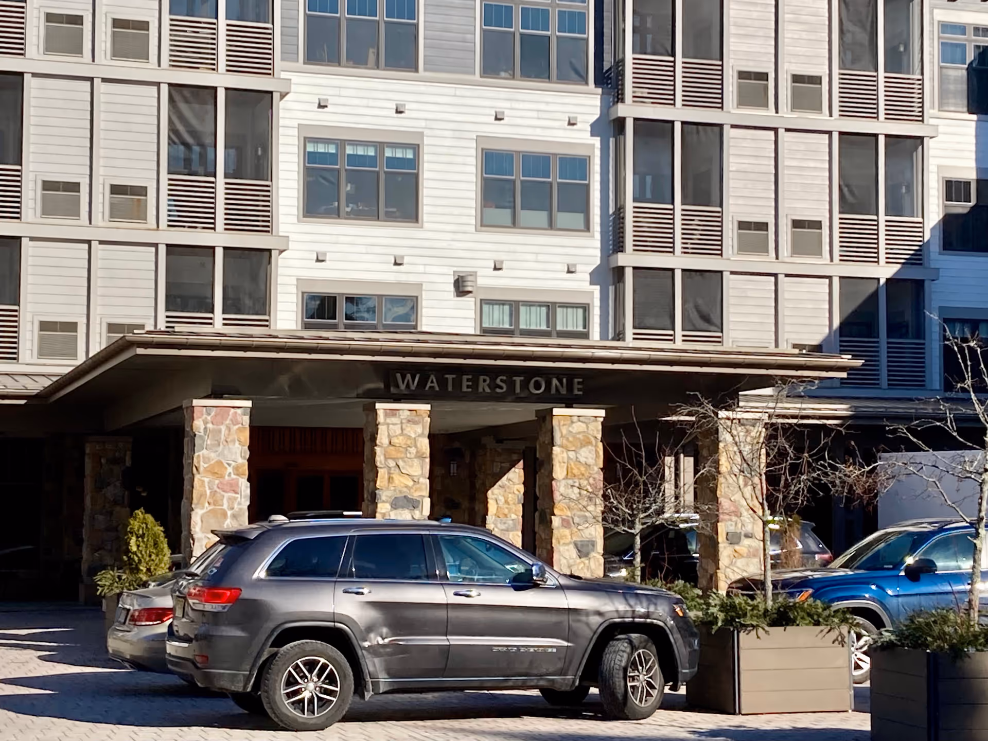 Entrance of the Waterstone at Wellesley building with a canopy reading "WATERSTONE", stone columns, and cars parked in front.