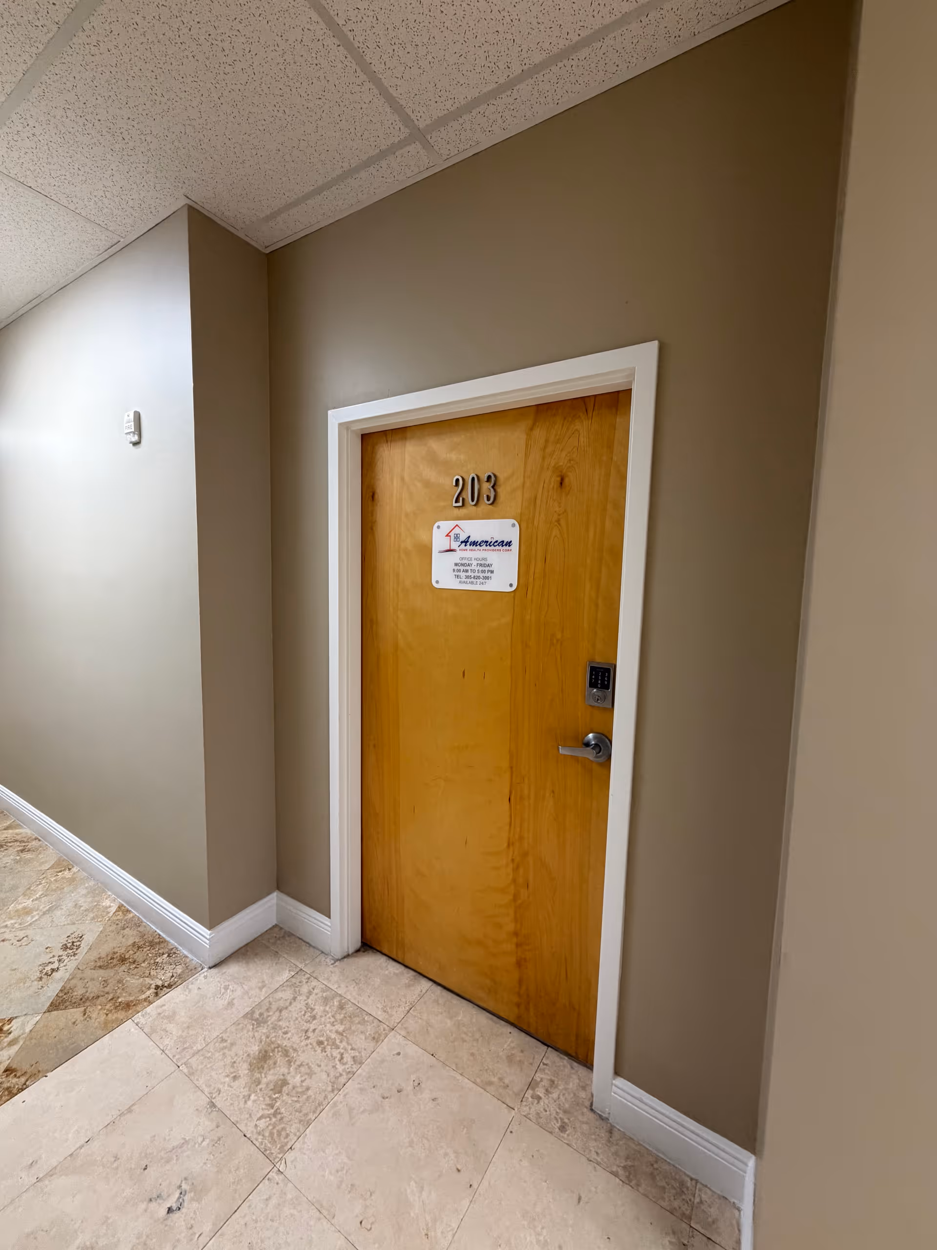 An interior hallway with a wooden door marked 203, beige walls, and tiled floor.