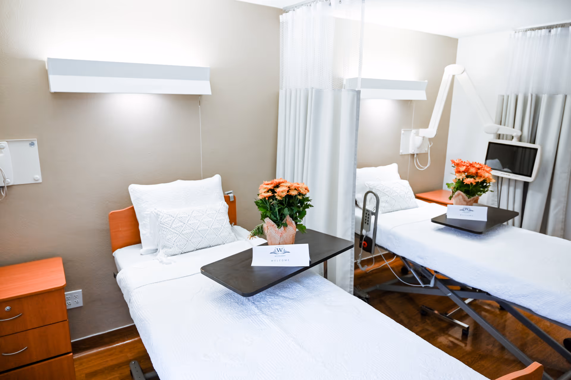 Two hospital-style beds with white bedding and privacy curtains in a patient room.
