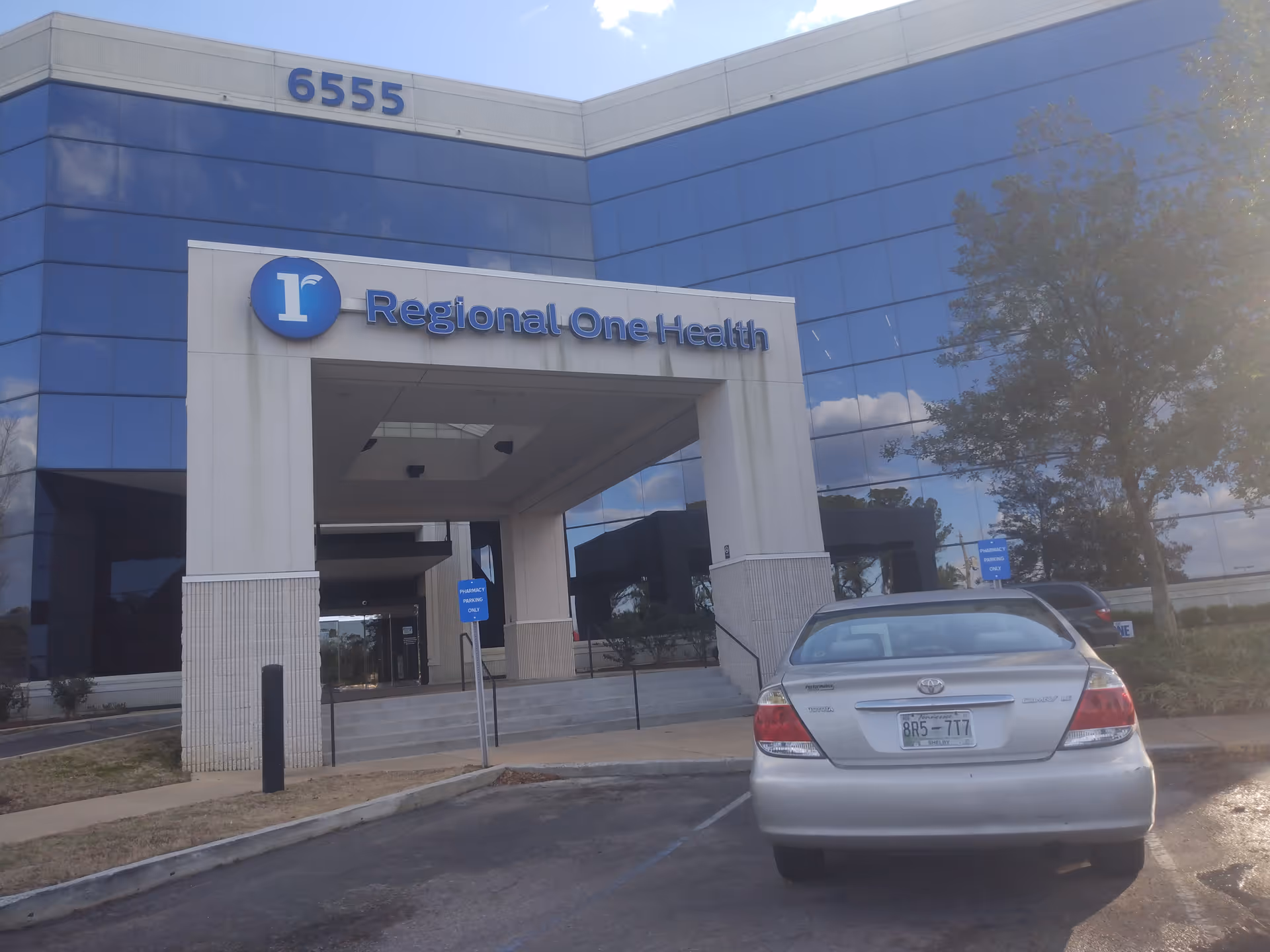 Blue glass-front Regional One Health building with entrance canopy and a parked car
