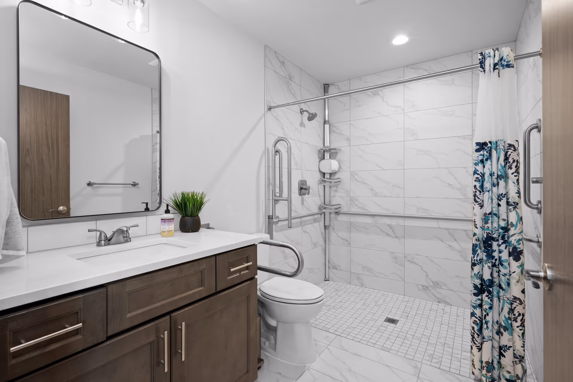 Accessible bathroom with vanity, mirror, toilet, shower, and grab bars.