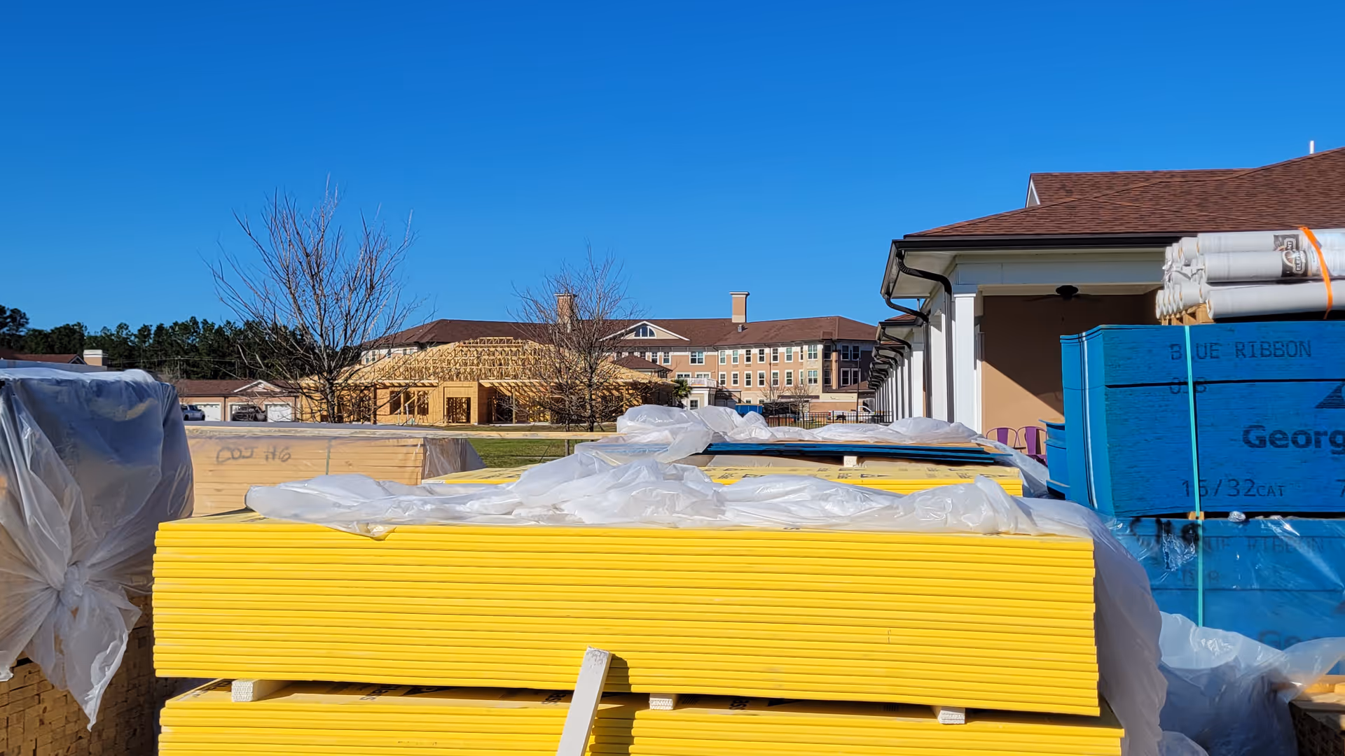 Construction materials and stacked yellow panels in foreground with Canterfield of Clay County building in distance