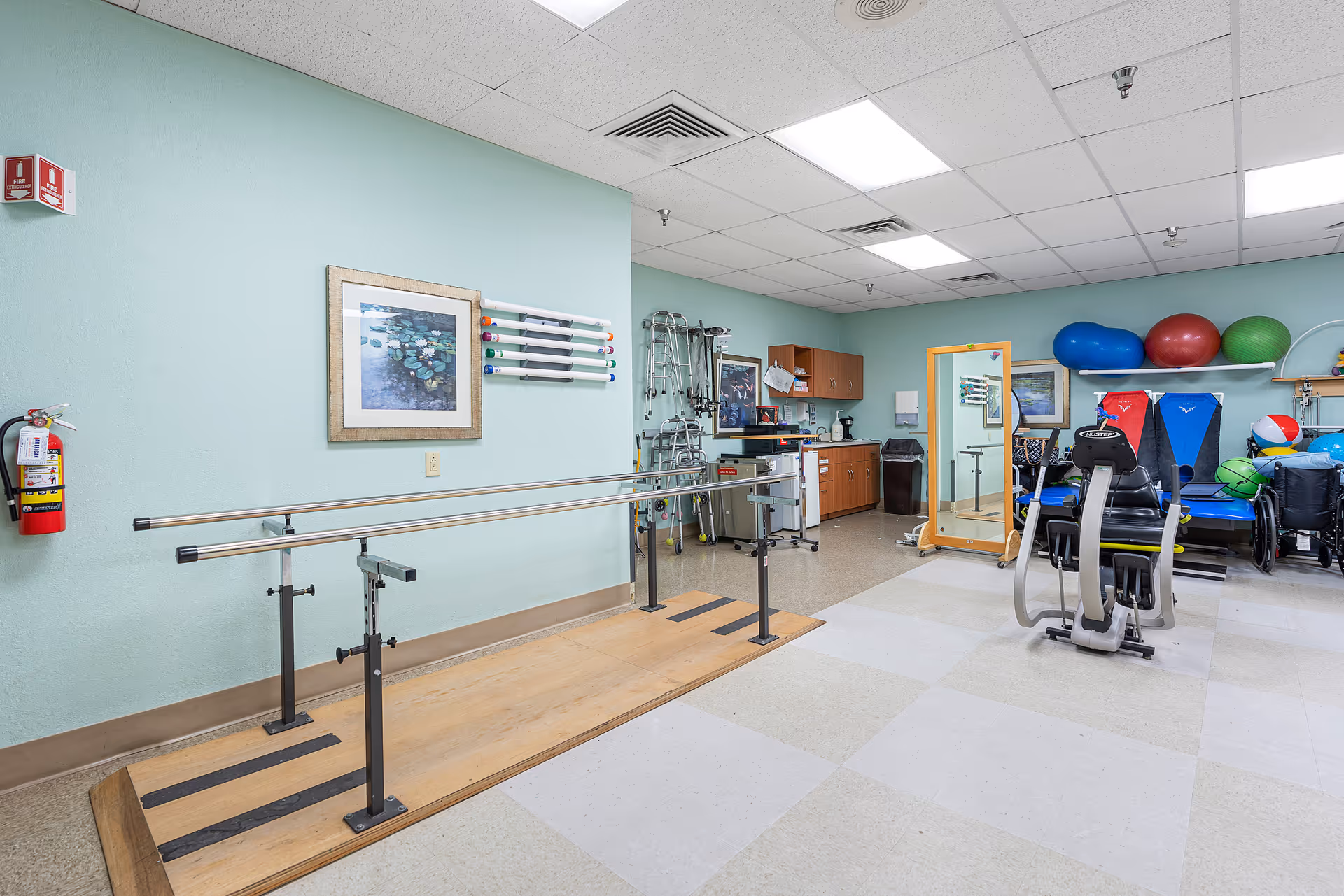 A rehabilitation gym with parallel bars, exercise equipment, and a mirror inside a therapy room.