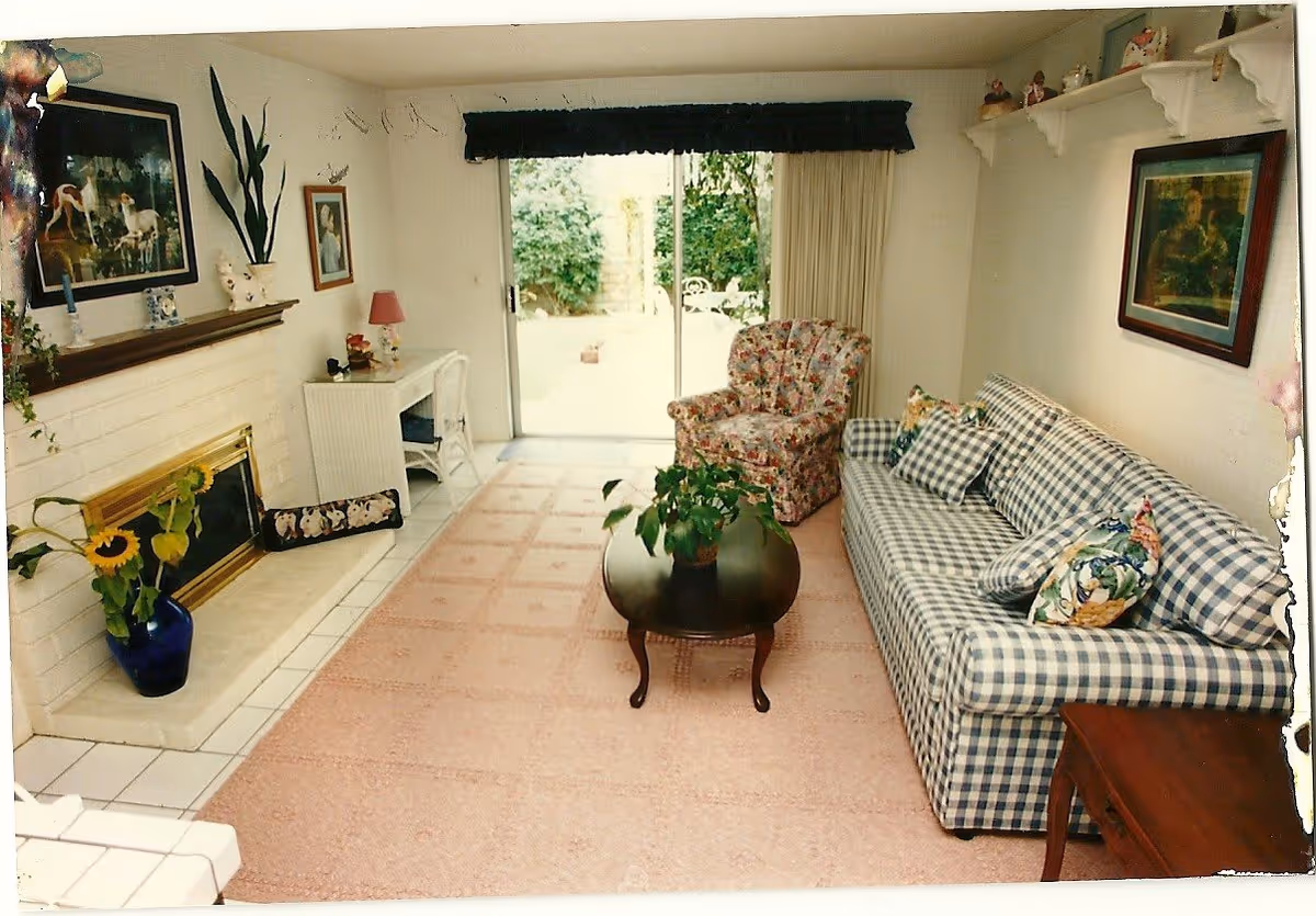 Cozy living room with checkered sofa, floral chairs, coffee table, fireplace, and sliding door to outdoors.
