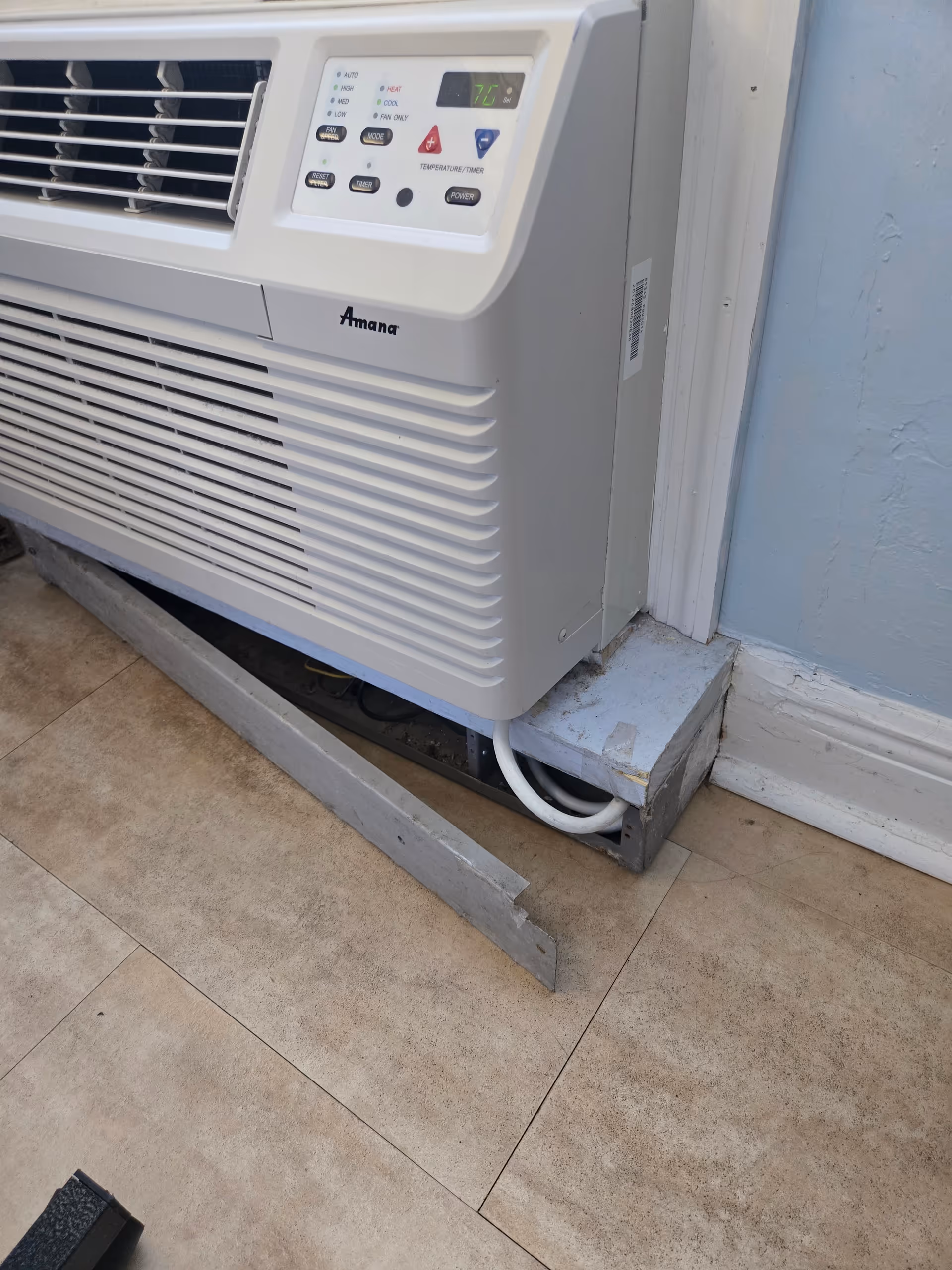 A wall-mounted Amana air conditioner unit in a blue-walled interior room.
