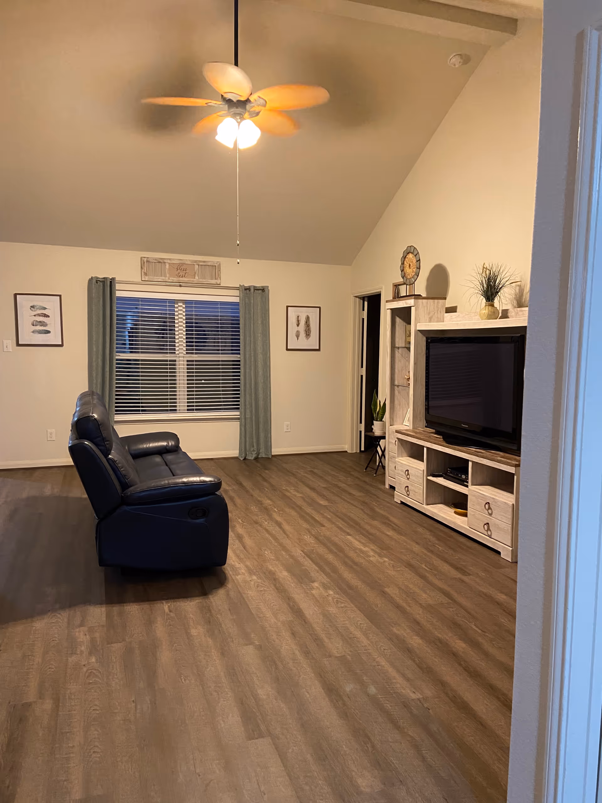 A cozy living room in a senior facility with a recliner, TV stand, and ceiling fan.