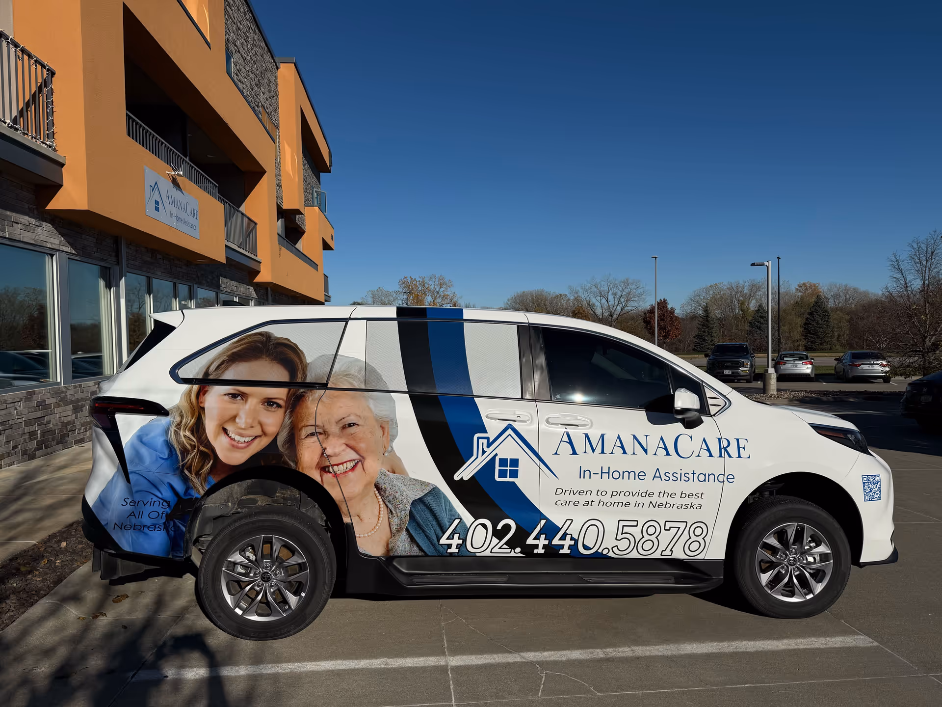 An AmanaCare van with smiling seniors graphic parked beside an orange building.