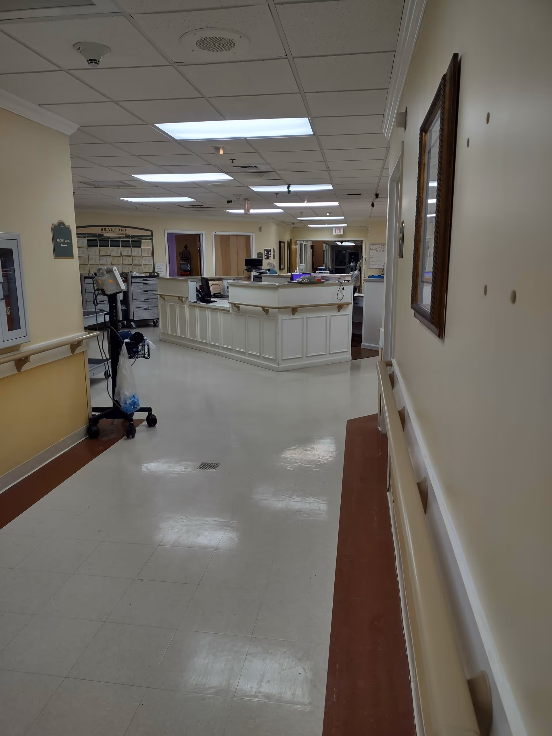 Nursing station at center of hallway in a senior living facility with beige walls.