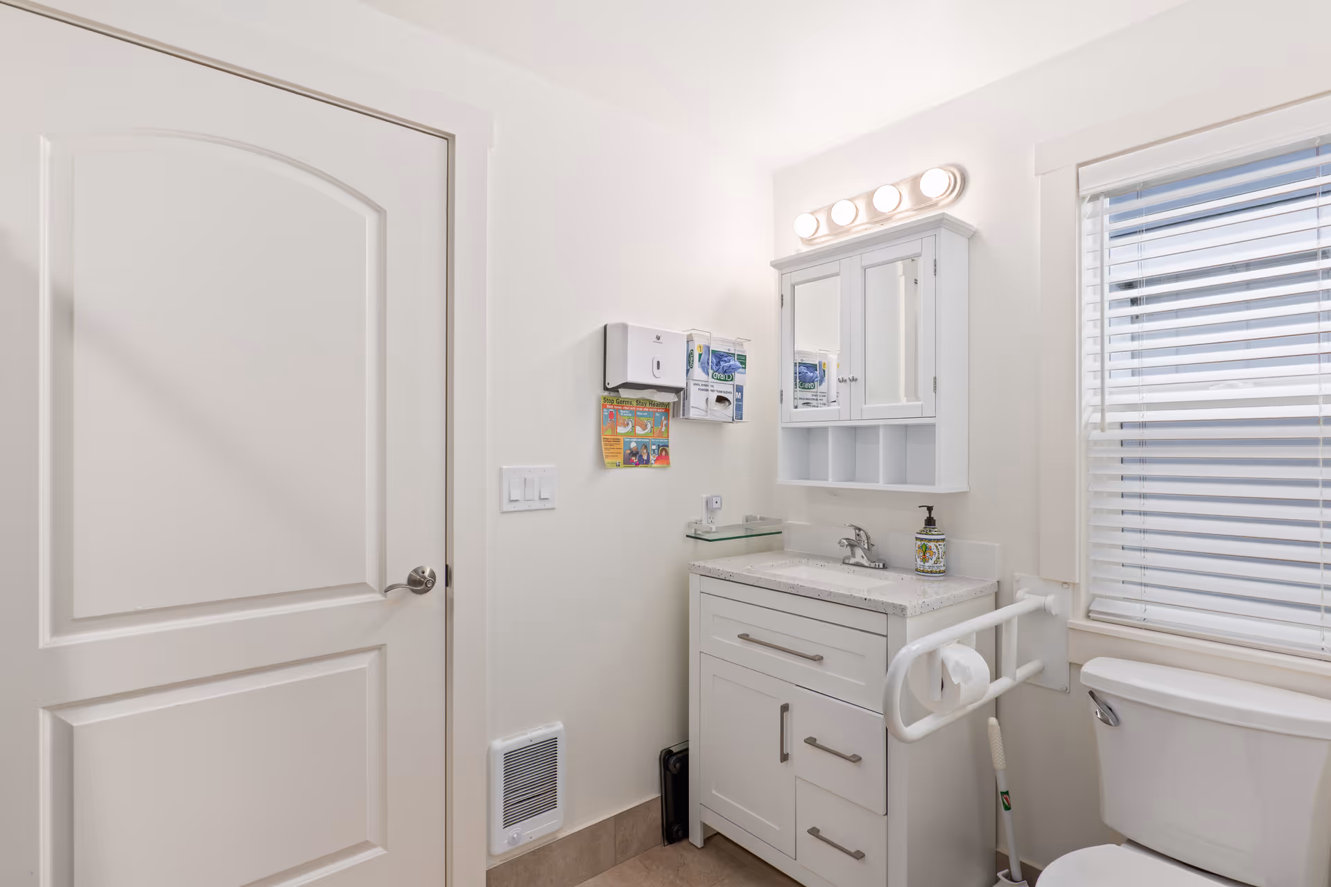 Bright white bathroom with sink vanity, mirror cabinet, grab bar, toilet, and window.
