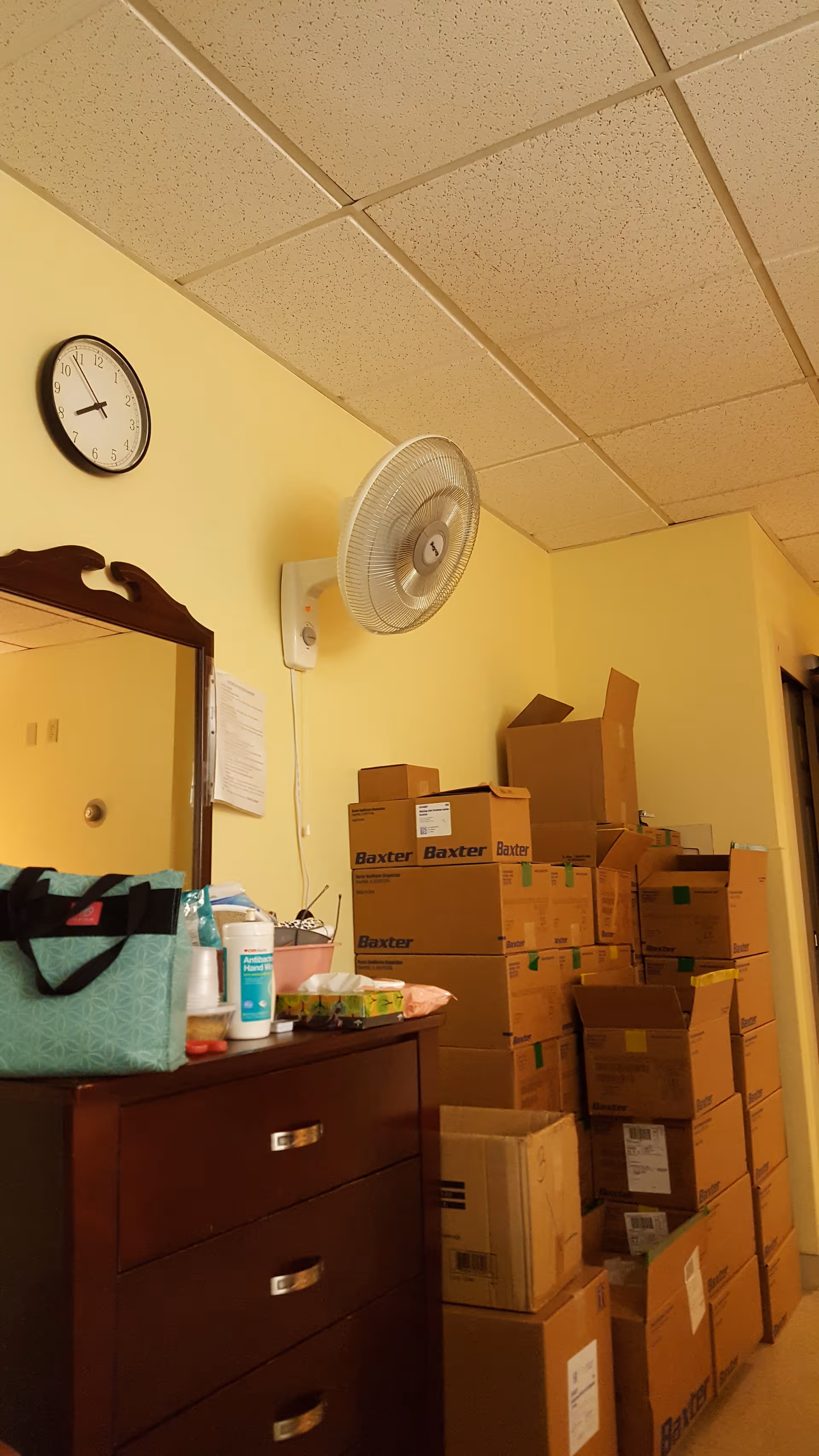 Yellow-walled interior storage room with stacked boxes, a dresser, and a wall clock.