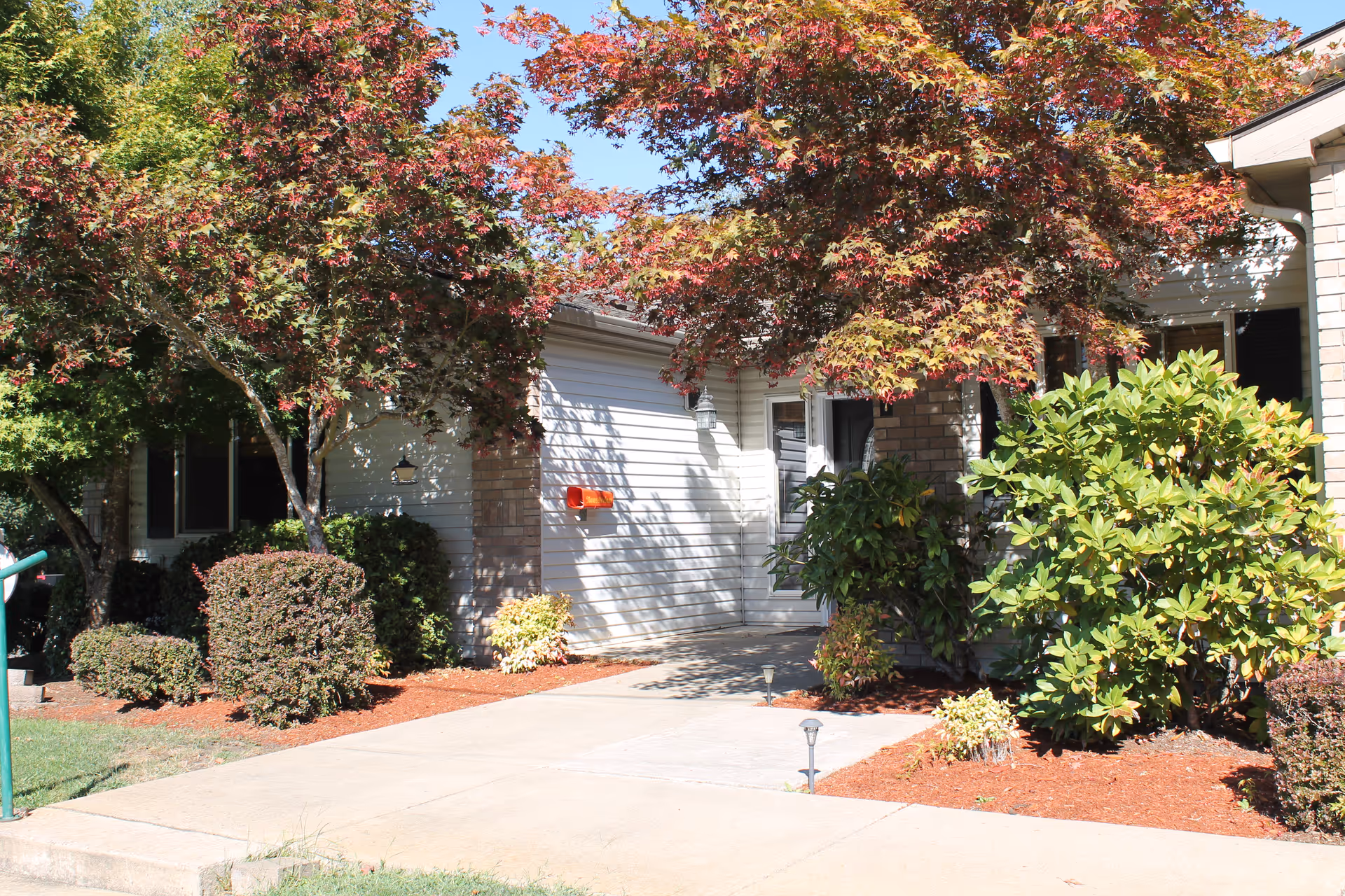 Exterior view of a senior living facility entrance with ramp and landscaped front yard.