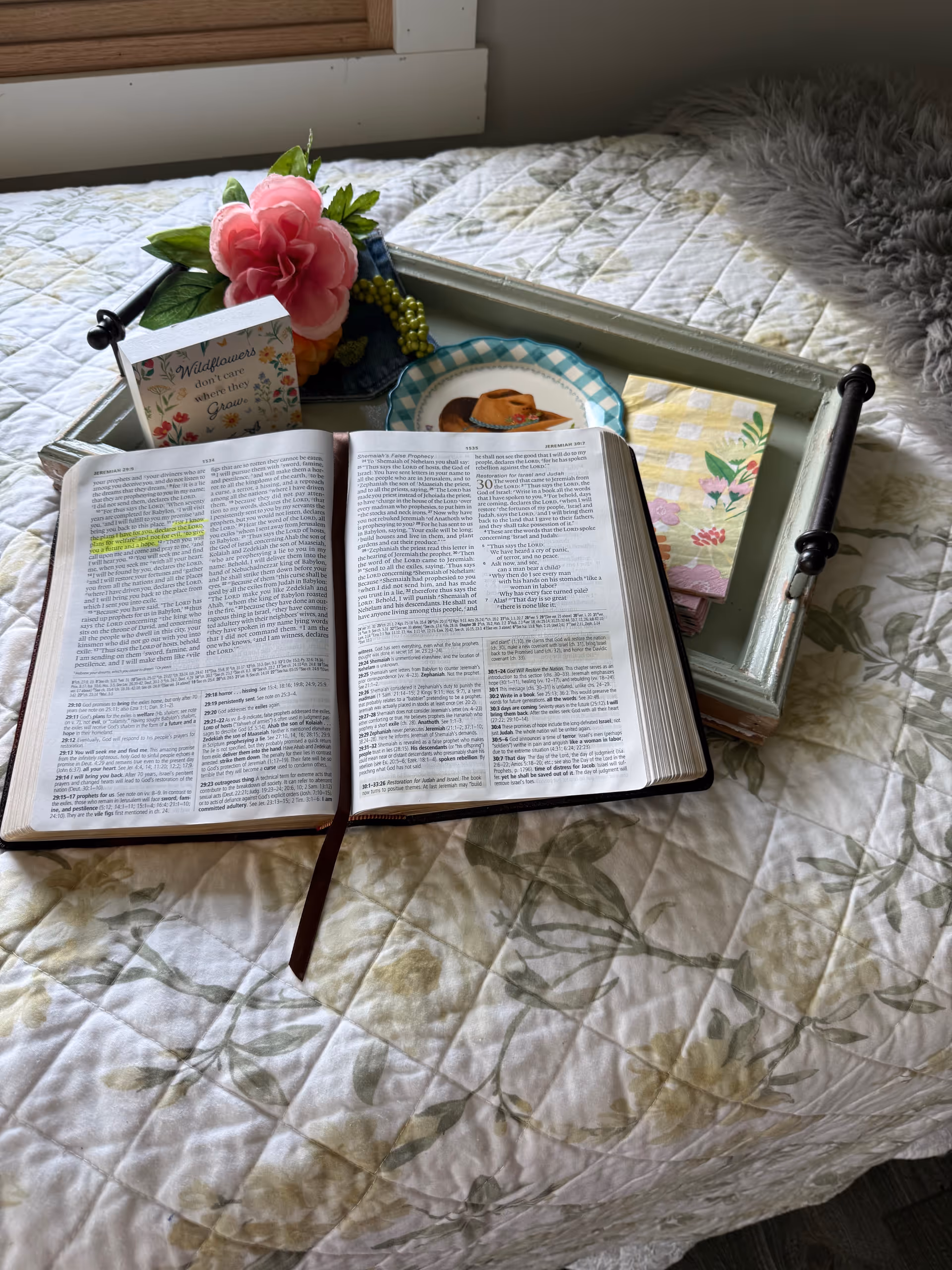 Open Bible on a bed with a decorative tray, flowers, and greeting cards.