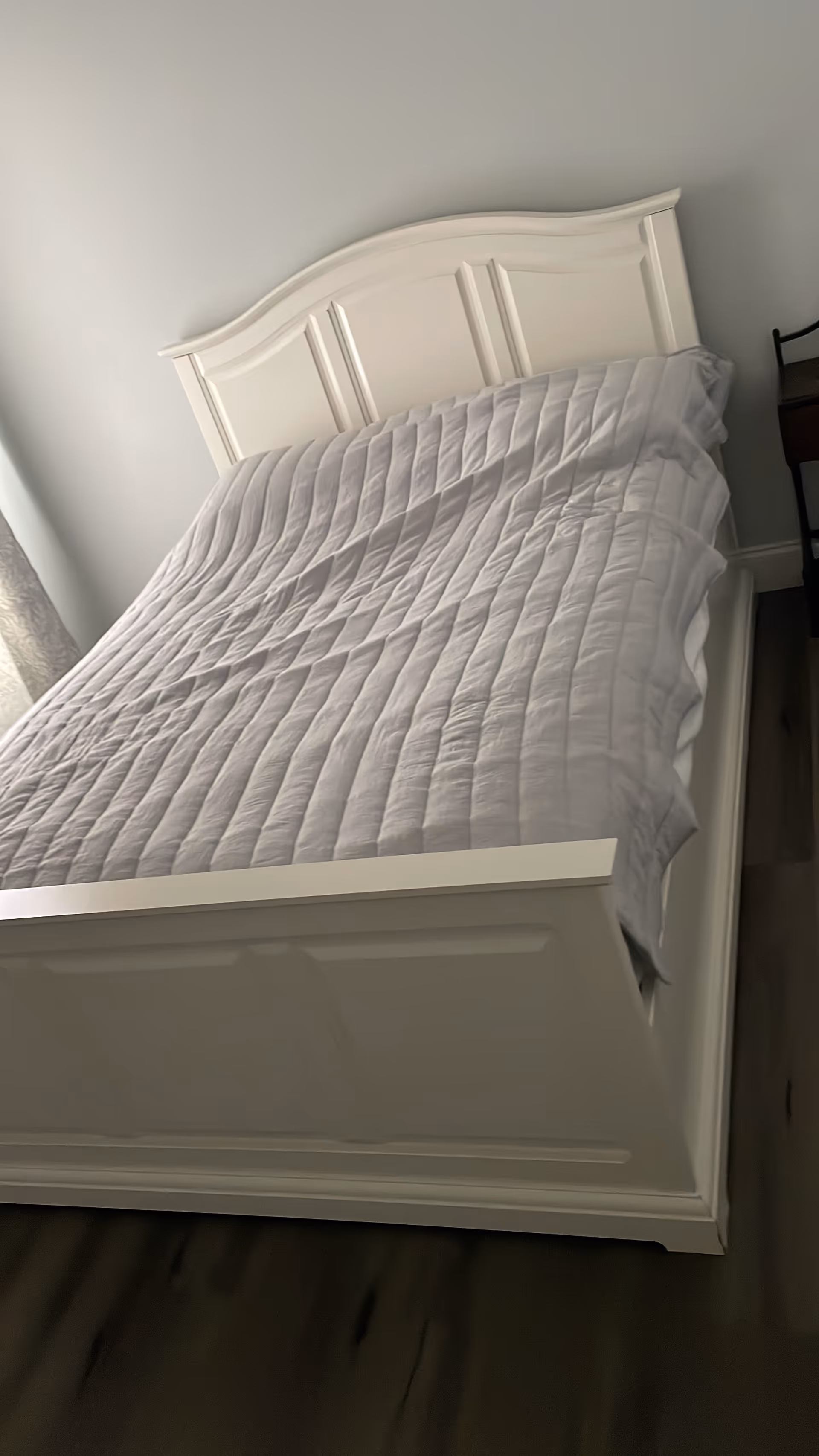 White bed with curved headboard and gray quilted comforter in a bright bedroom.