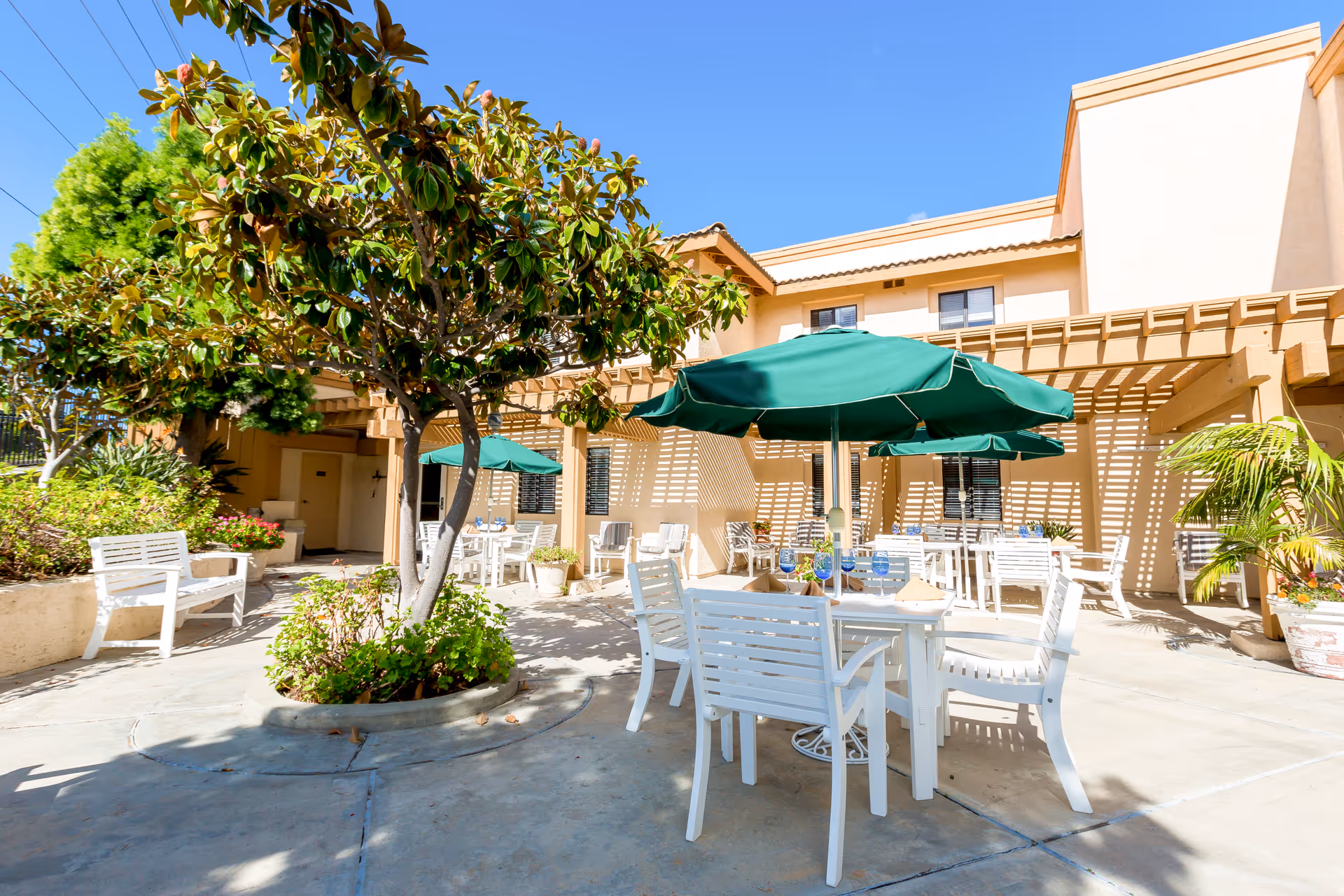 Sunny outdoor patio at Brookdale Senior Living with white furniture and green umbrellas.