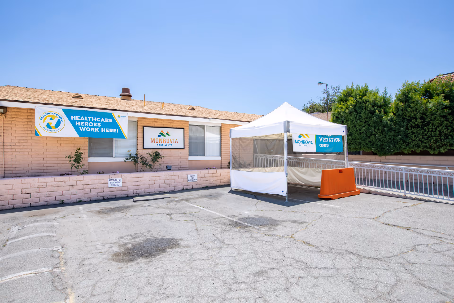 Exterior front of Monrovia Post Acute showing a white visitation tent in the parking area and banners reading 'Healthcare Heroes Work Here' and 'Monrovia'.