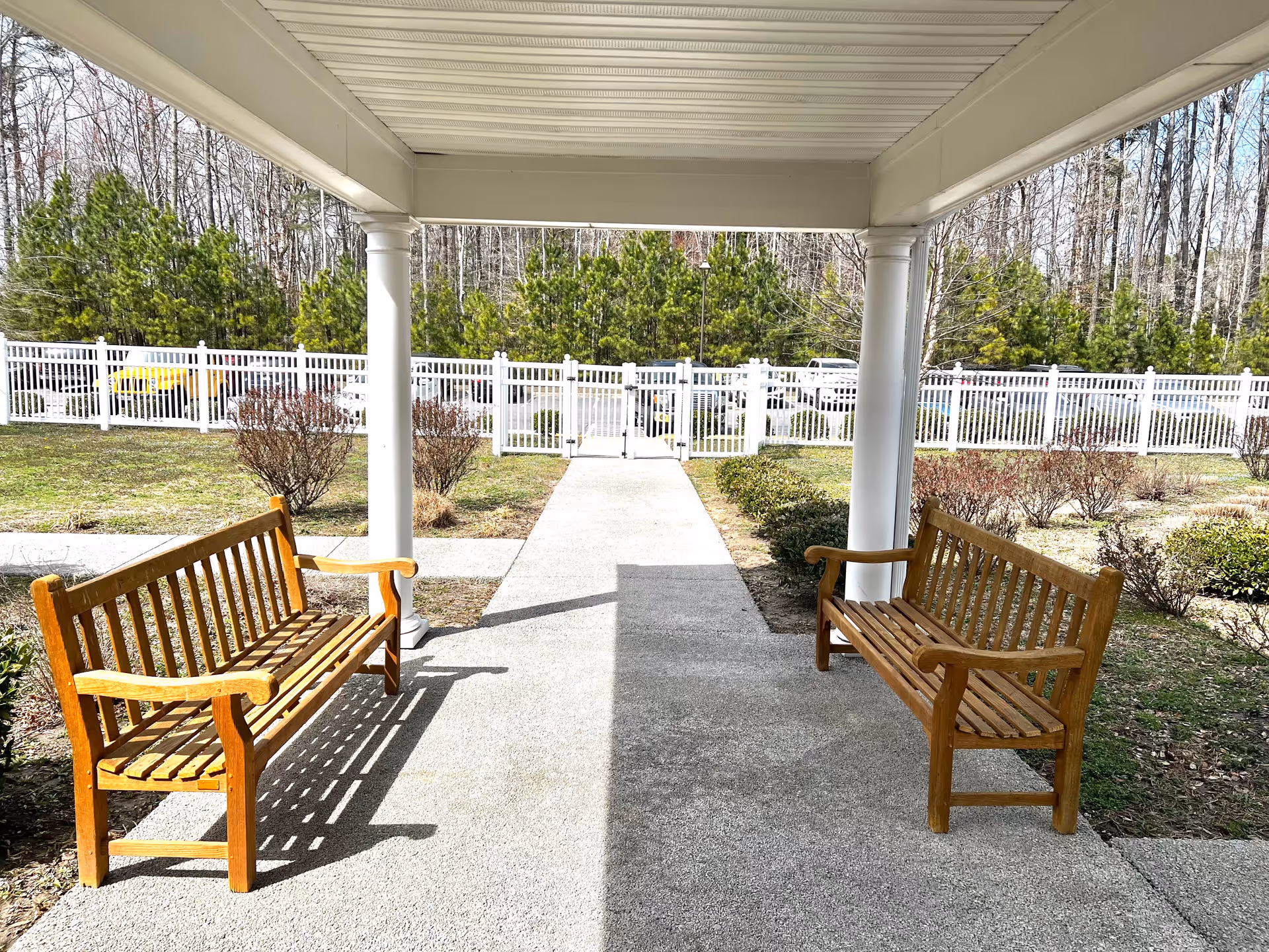 Two wooden benches under a covered walkway flank a central concrete path.