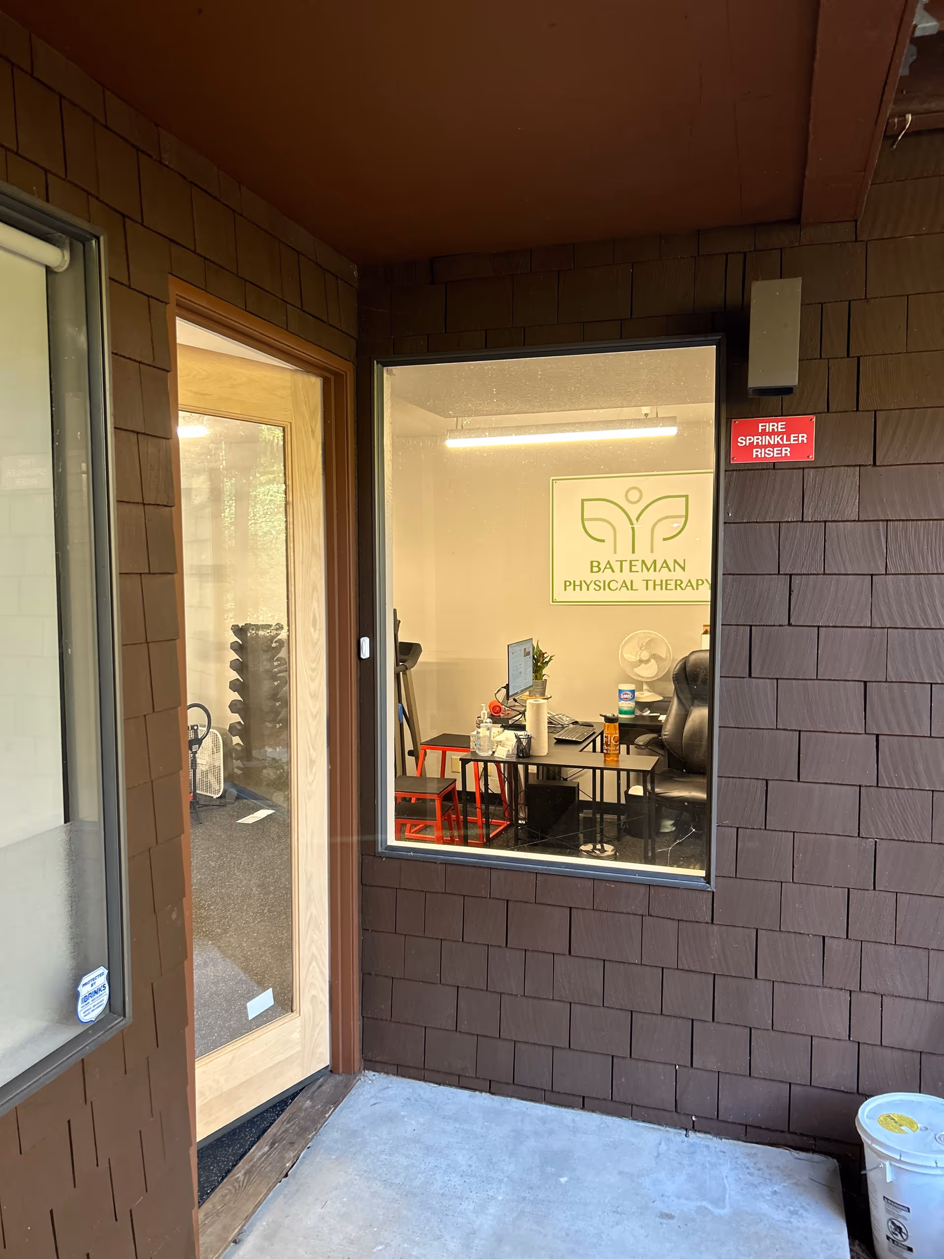Exterior wall with window into Bateman Physical Therapy office showing a desk.