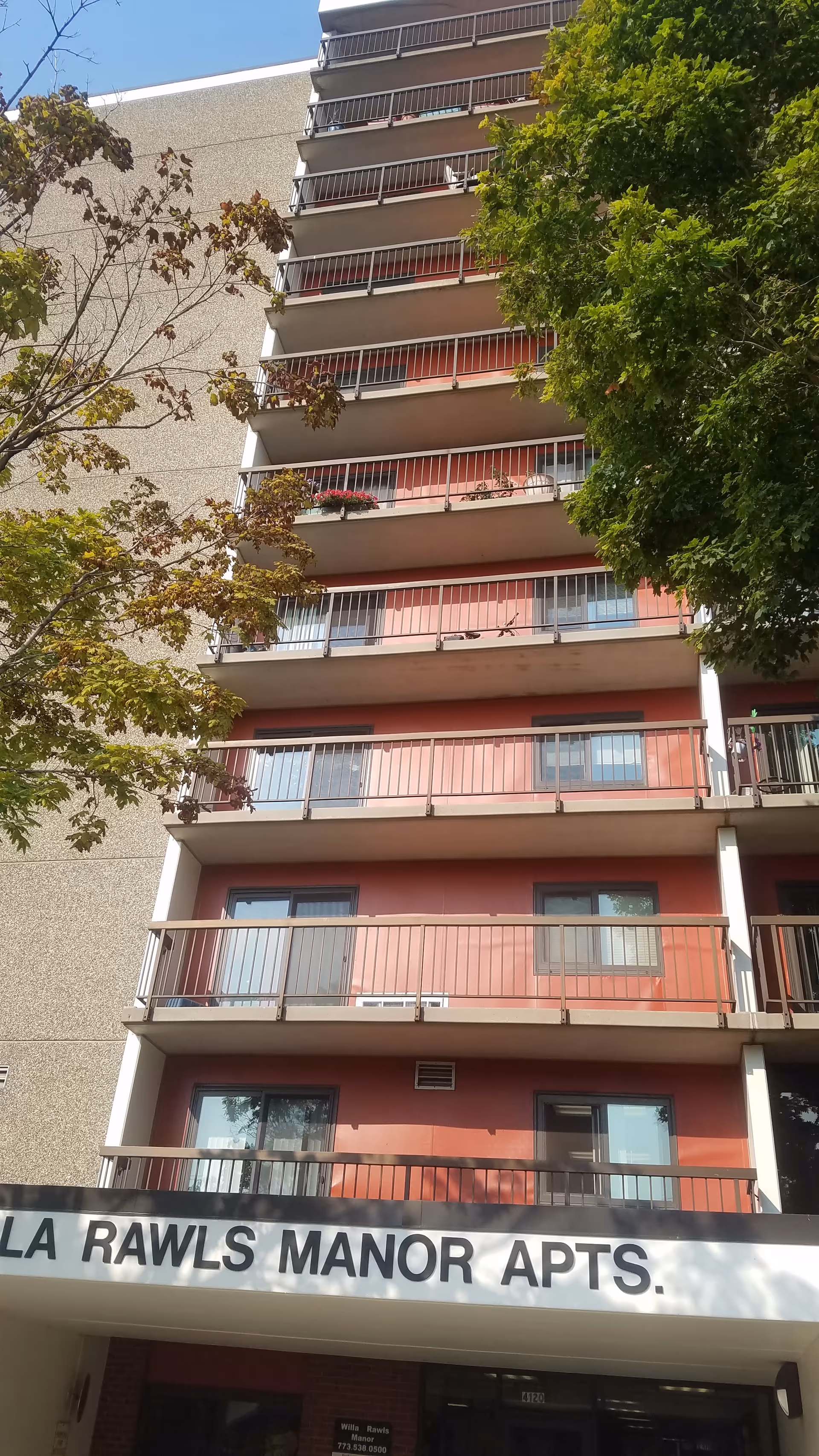 Tall apartment building with red balconies and nearby trees.