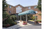 Exterior view of Sayre Christian Village entrance with brick building, glass doors, and a teal canopy.