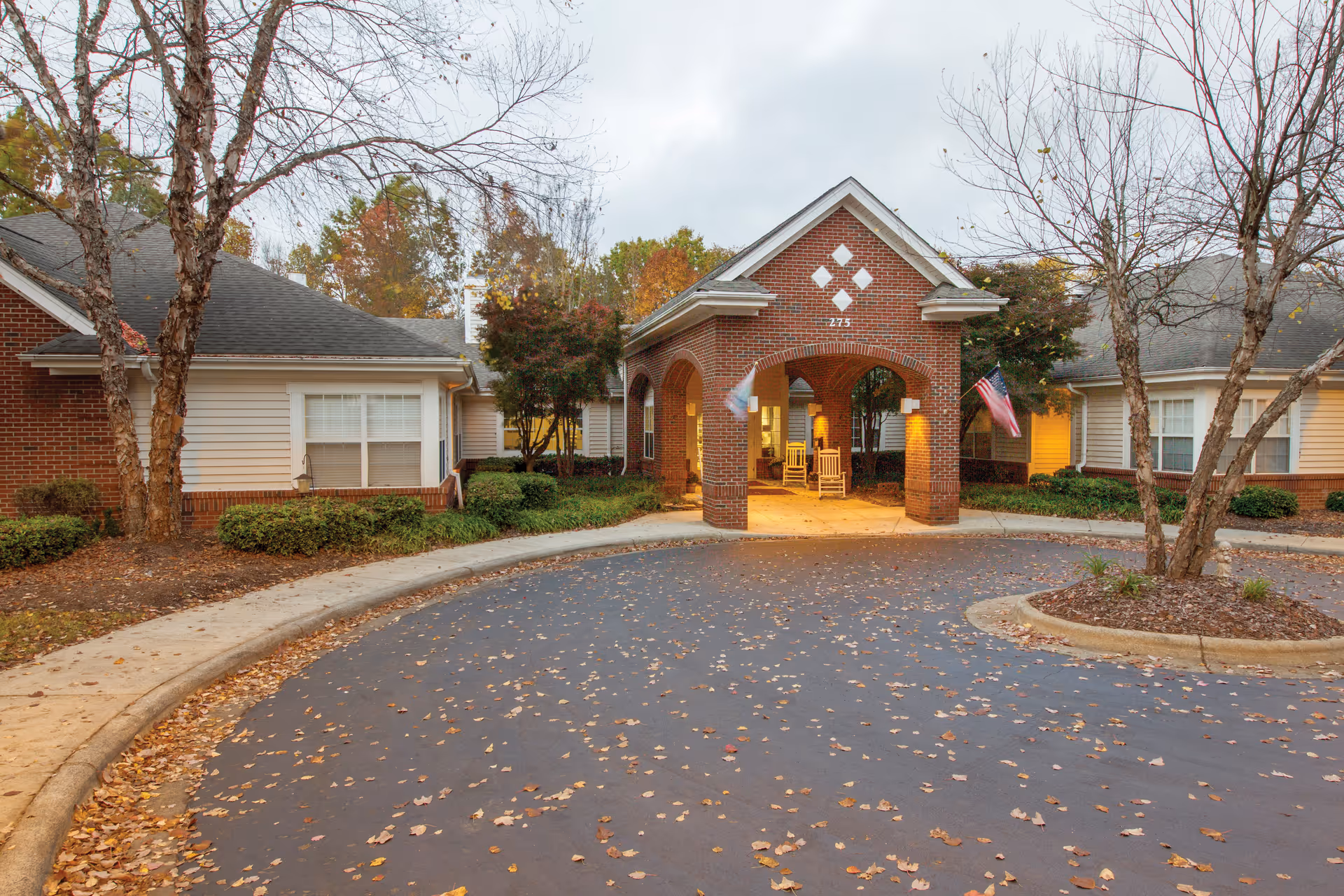 Brick senior living facility entrance with arched brick pillars and flagpoles.