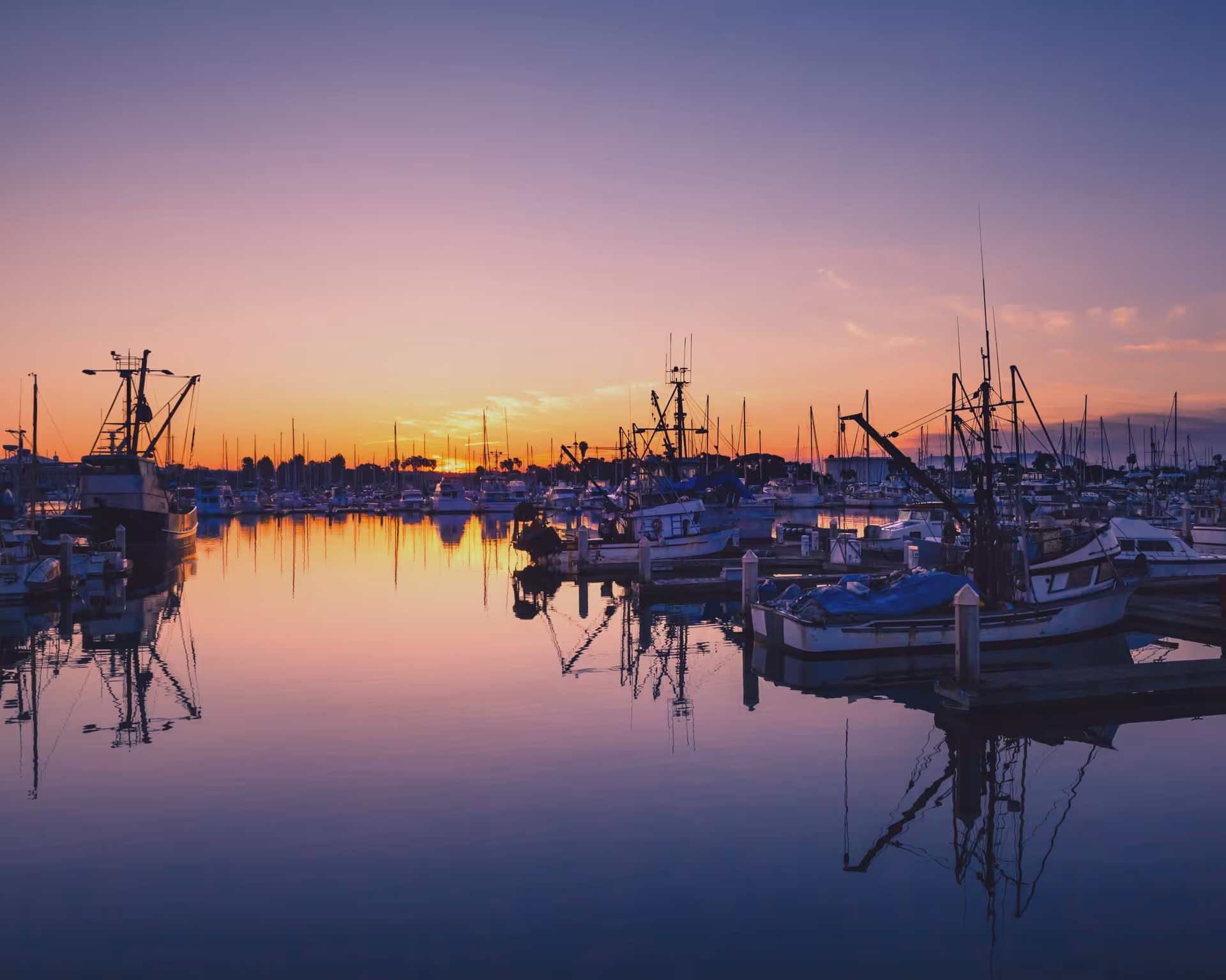 Sunset over a calm marina with numerous boats reflected in still water.