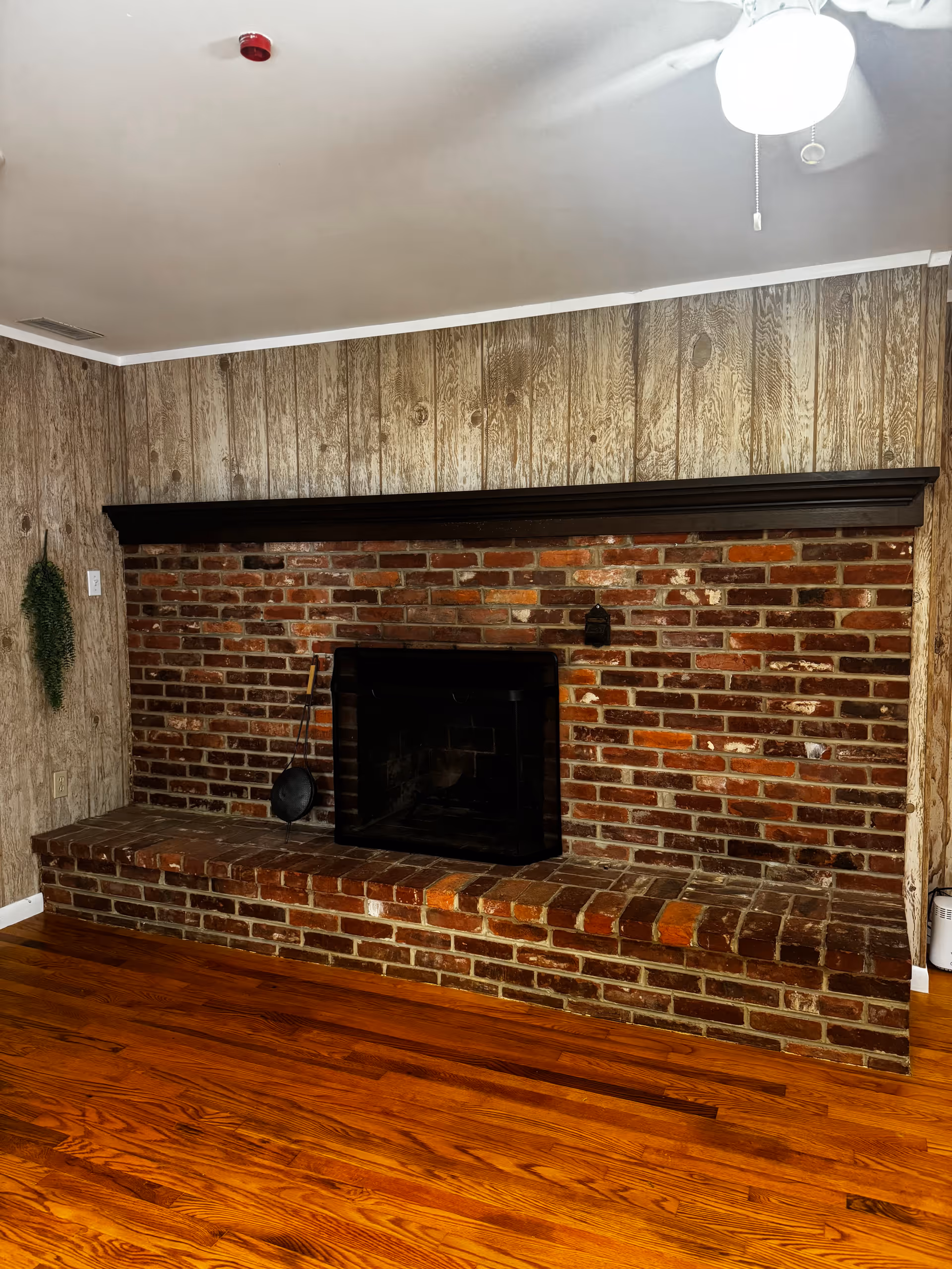 Brick fireplace with a wooden mantel and paneled walls in a simple interior.