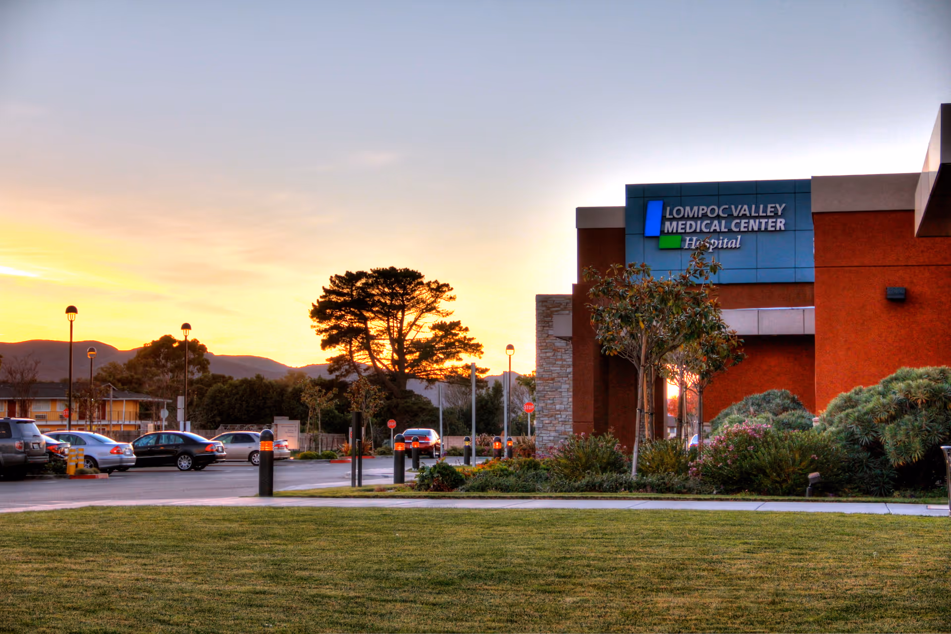 Exterior view of Lompoc Valley Medical Center with cars in parking lot at sunset.