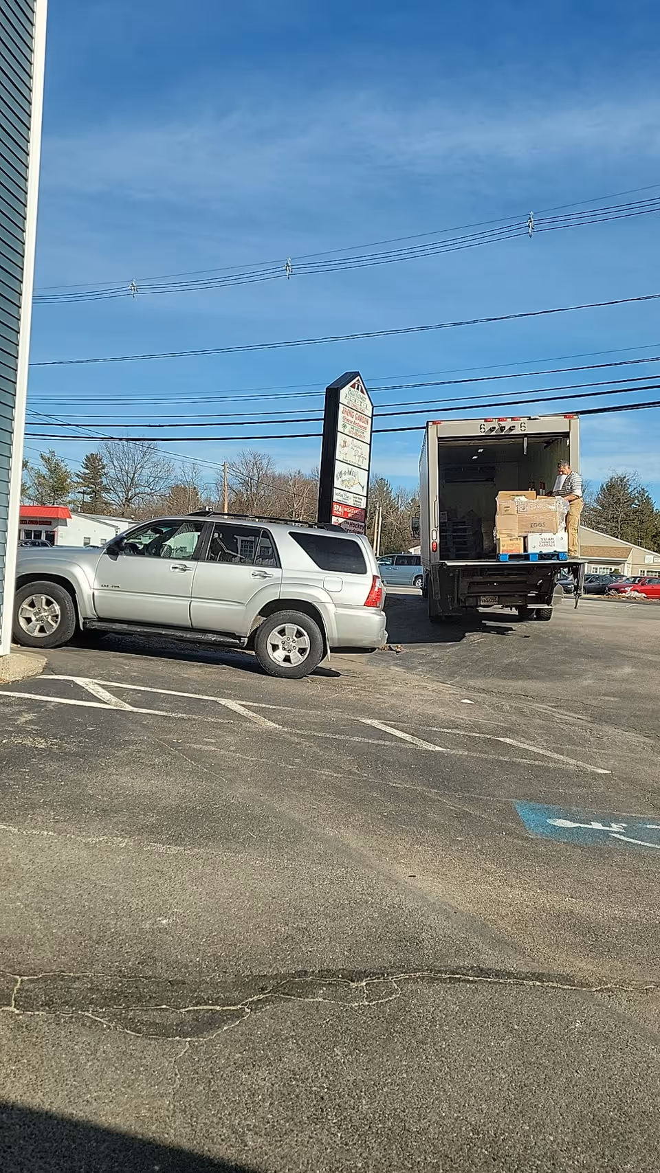 A delivery truck unloads boxes beside a parked SUV in a facility parking lot.