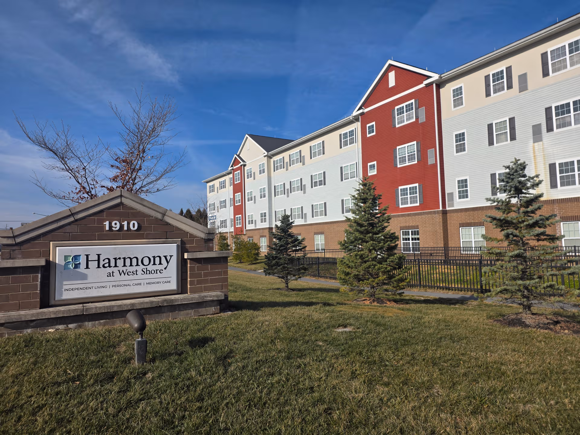 Exterior view of Harmony at West Shore senior living building with sign and landscaping.