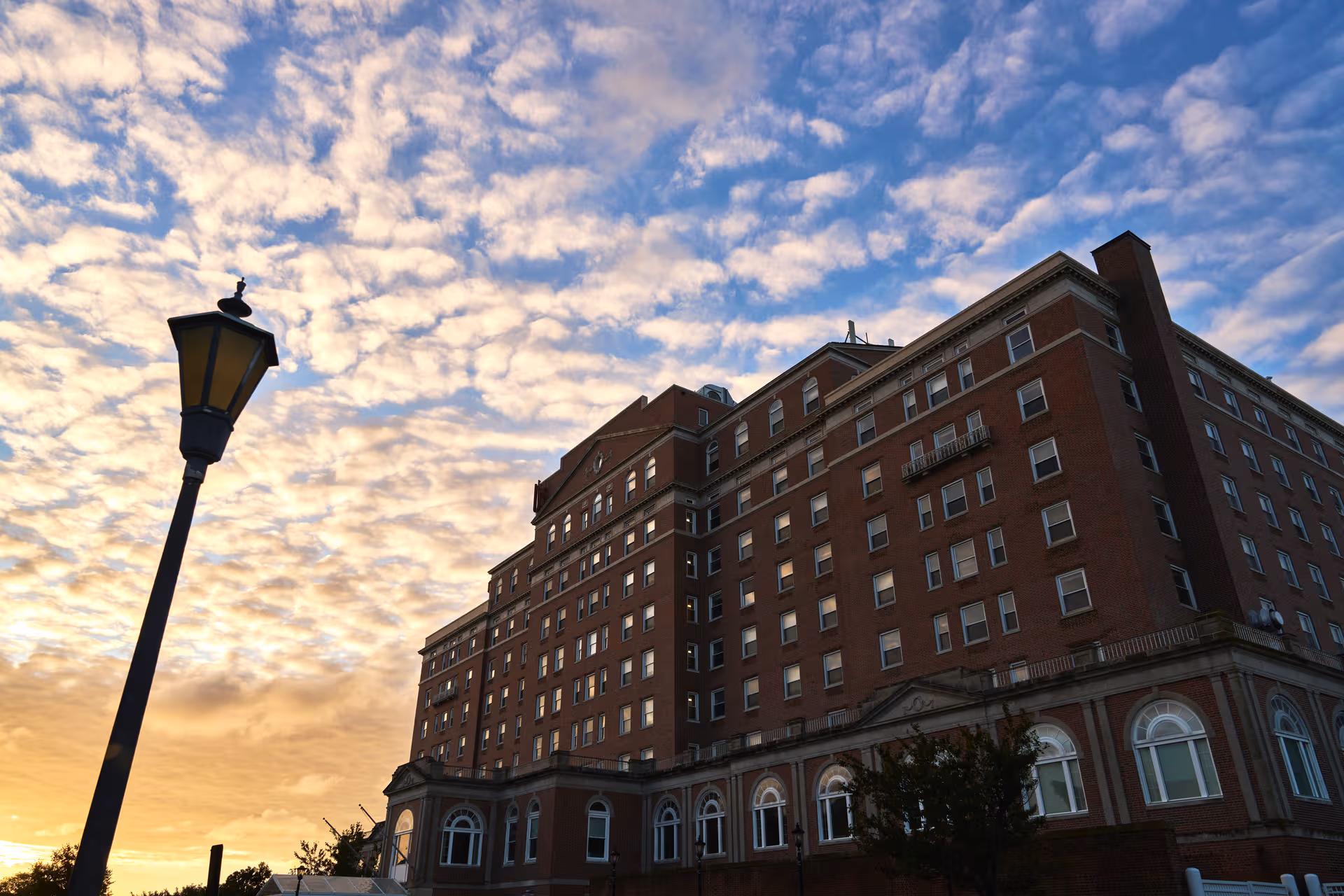 Tall brick senior living building rises beside a street lamp at sunset.