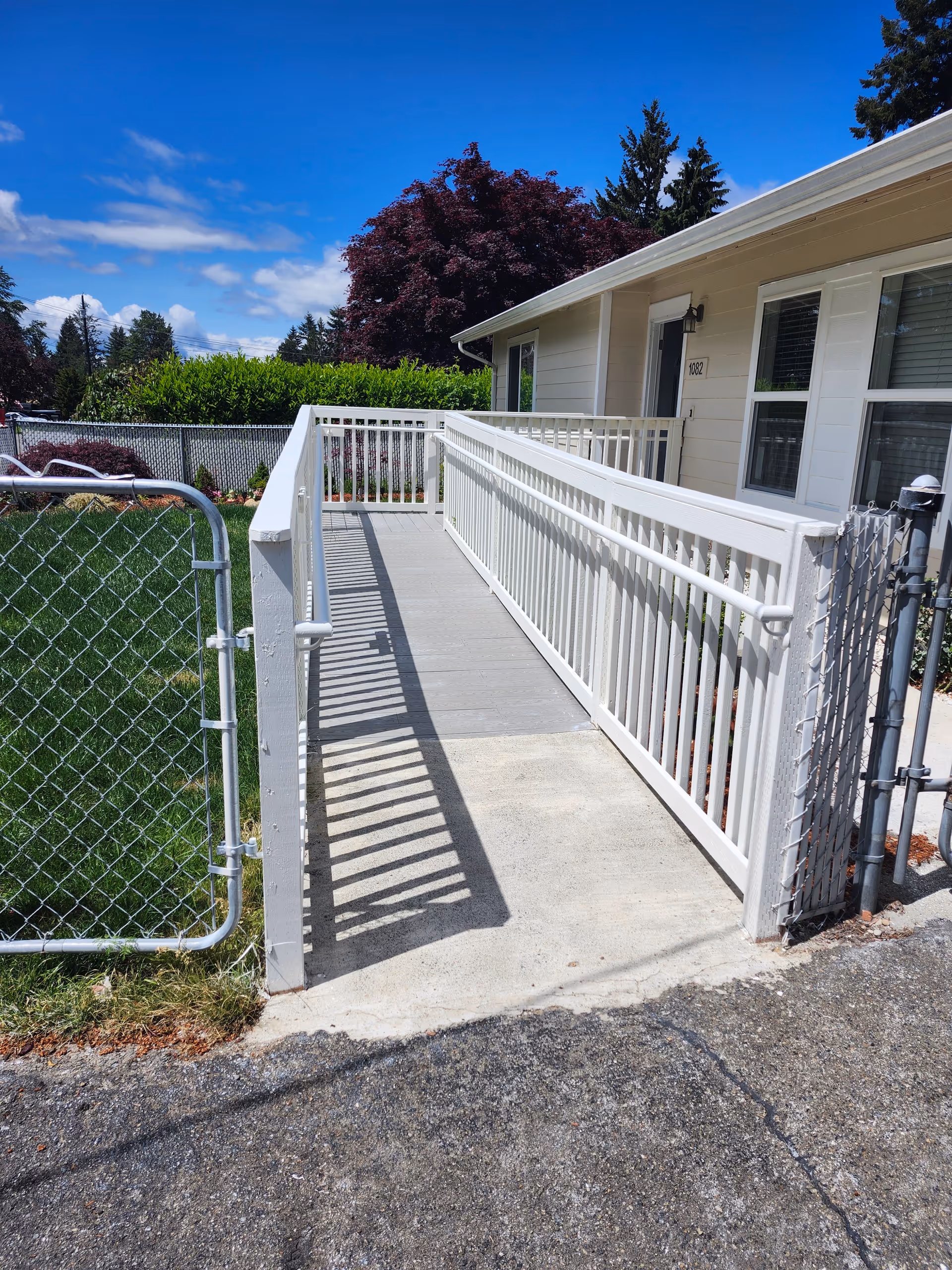 White ramp leads to a single-story home with a fenced yard and blue sky.