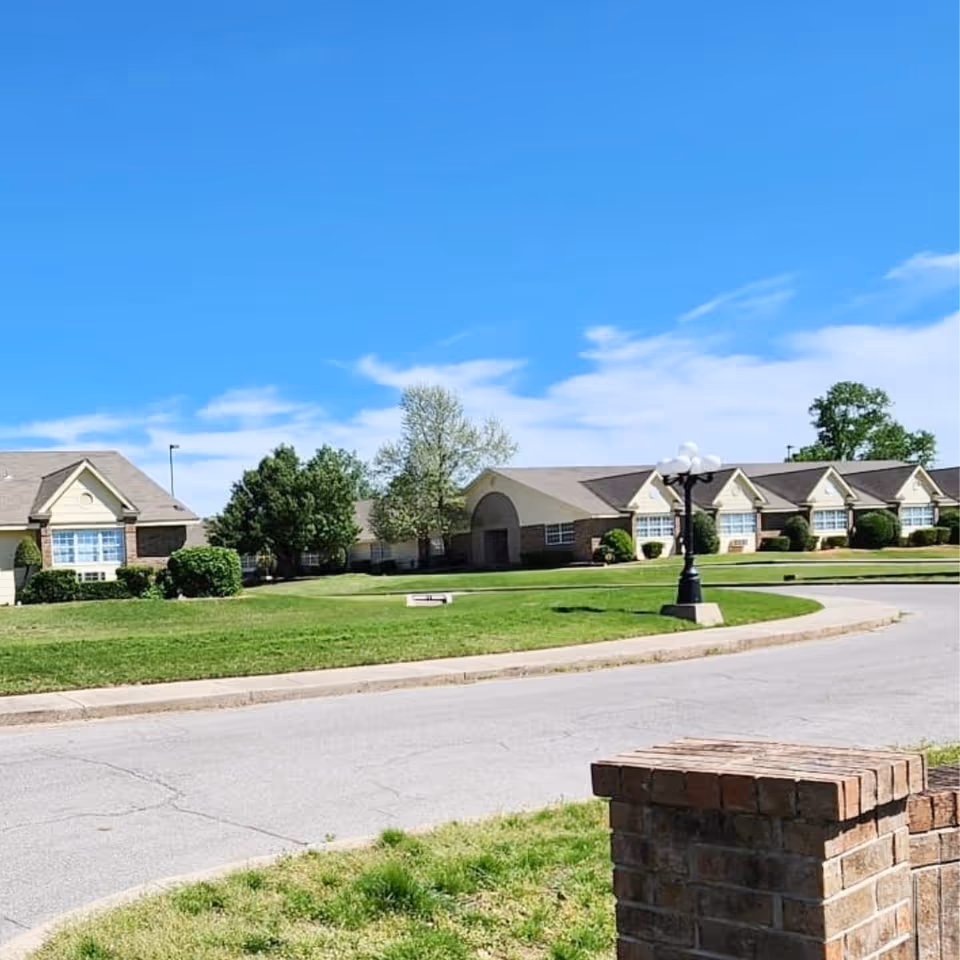 Single-story senior living facility with brick exterior, manicured lawn, and curved driveway.
