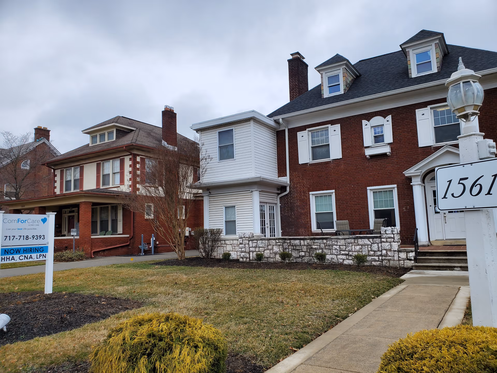 Exterior view of a brick senior home with a sign, sidewalk, and landscaping.
