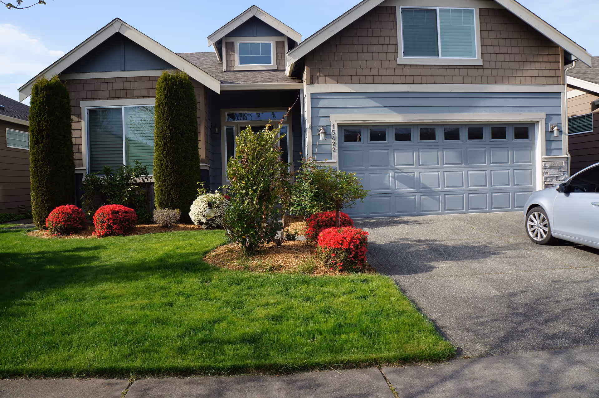 Front exterior of a single-family home with a two-car garage, manicured lawn, shrubs, and a parked silver car.