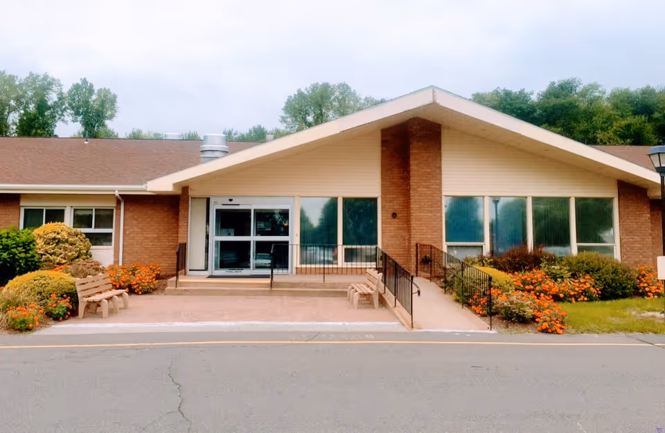 Brick single-story senior facility entrance with glass doors and landscaped shrubs along the front