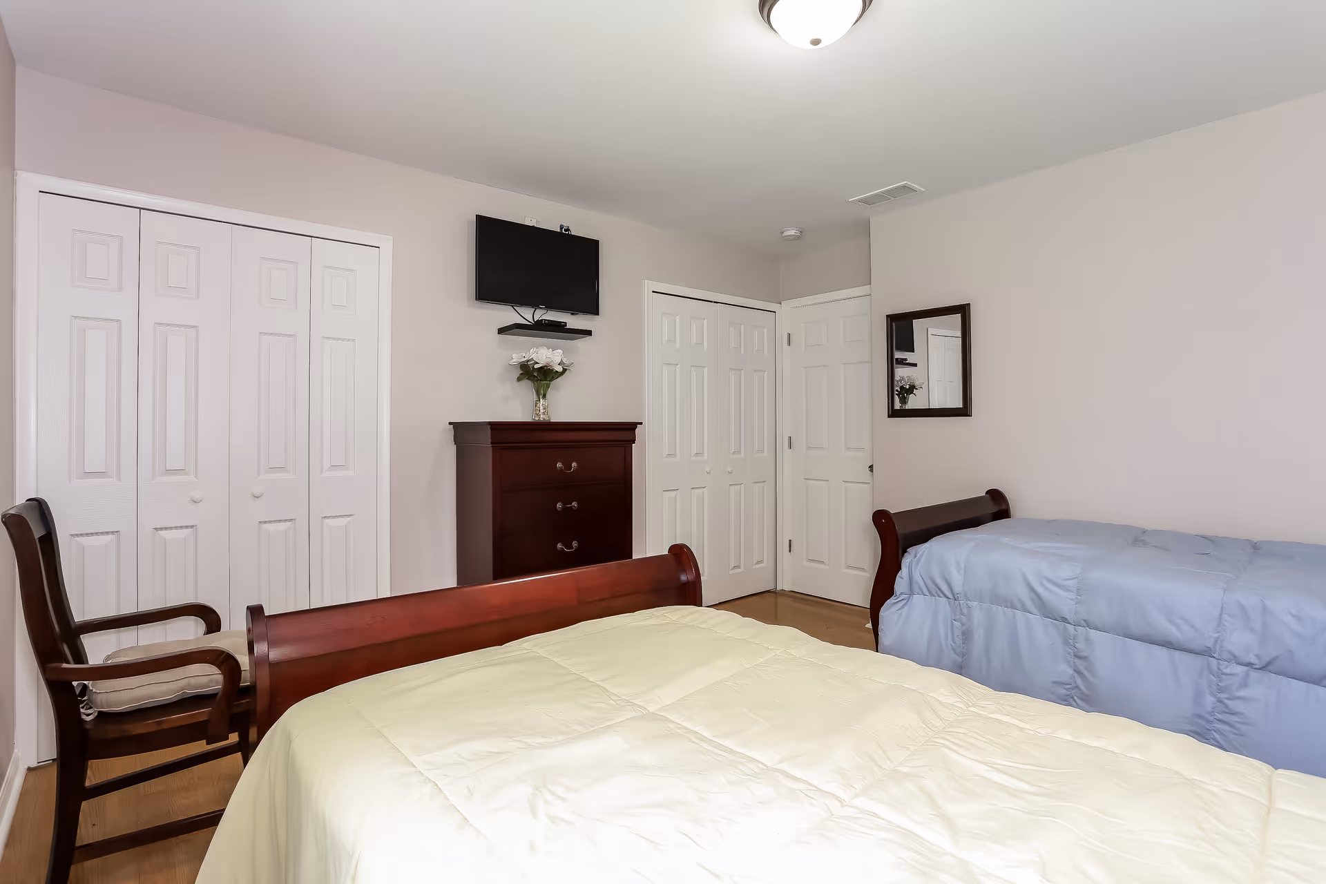 Two twin beds with wooden frames, dresser, wall-mounted TV, and closet doors in a bedroom.