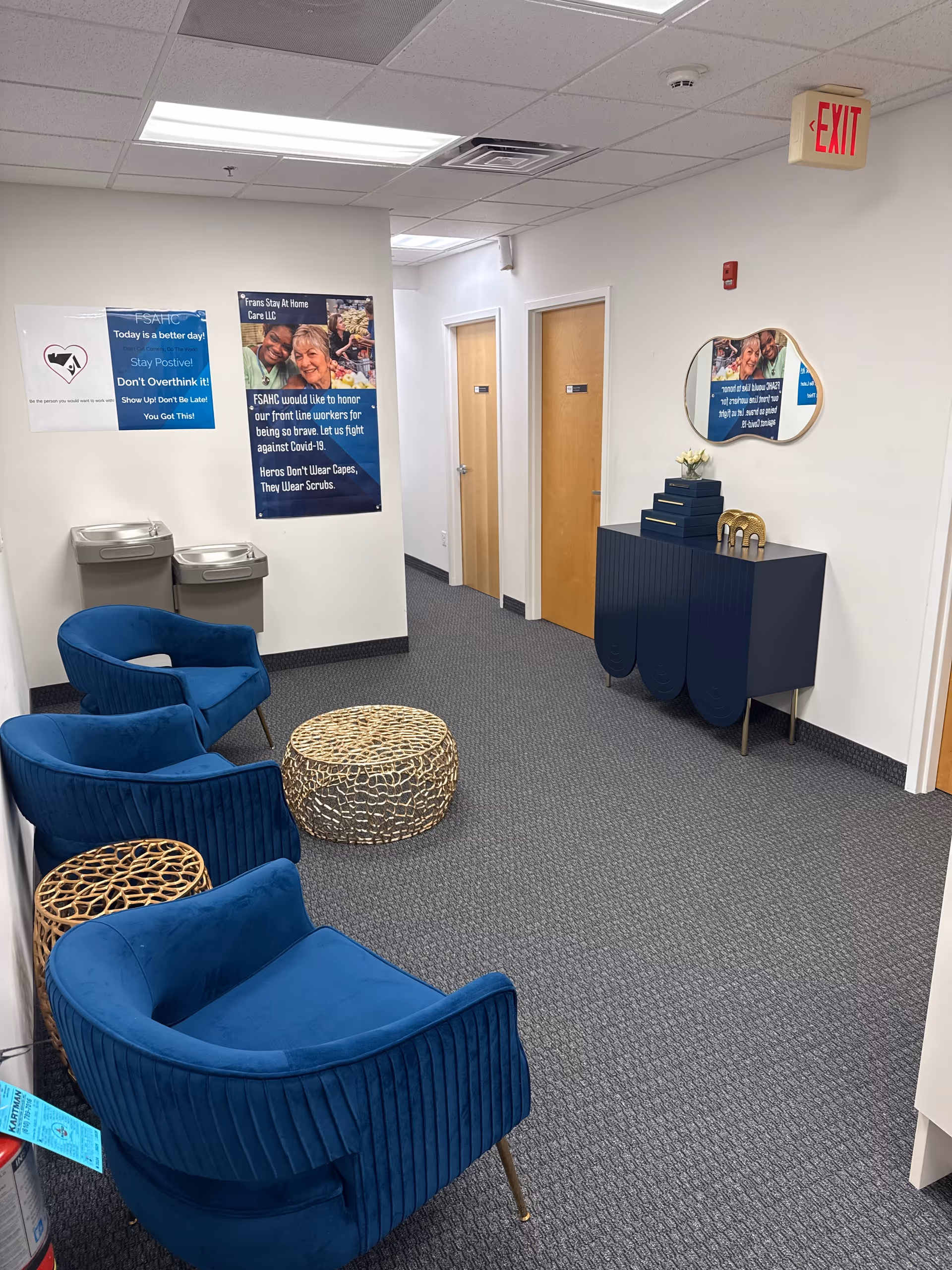 A waiting area with blue chairs, wicker tables, posters, and a reception cabinet inside.