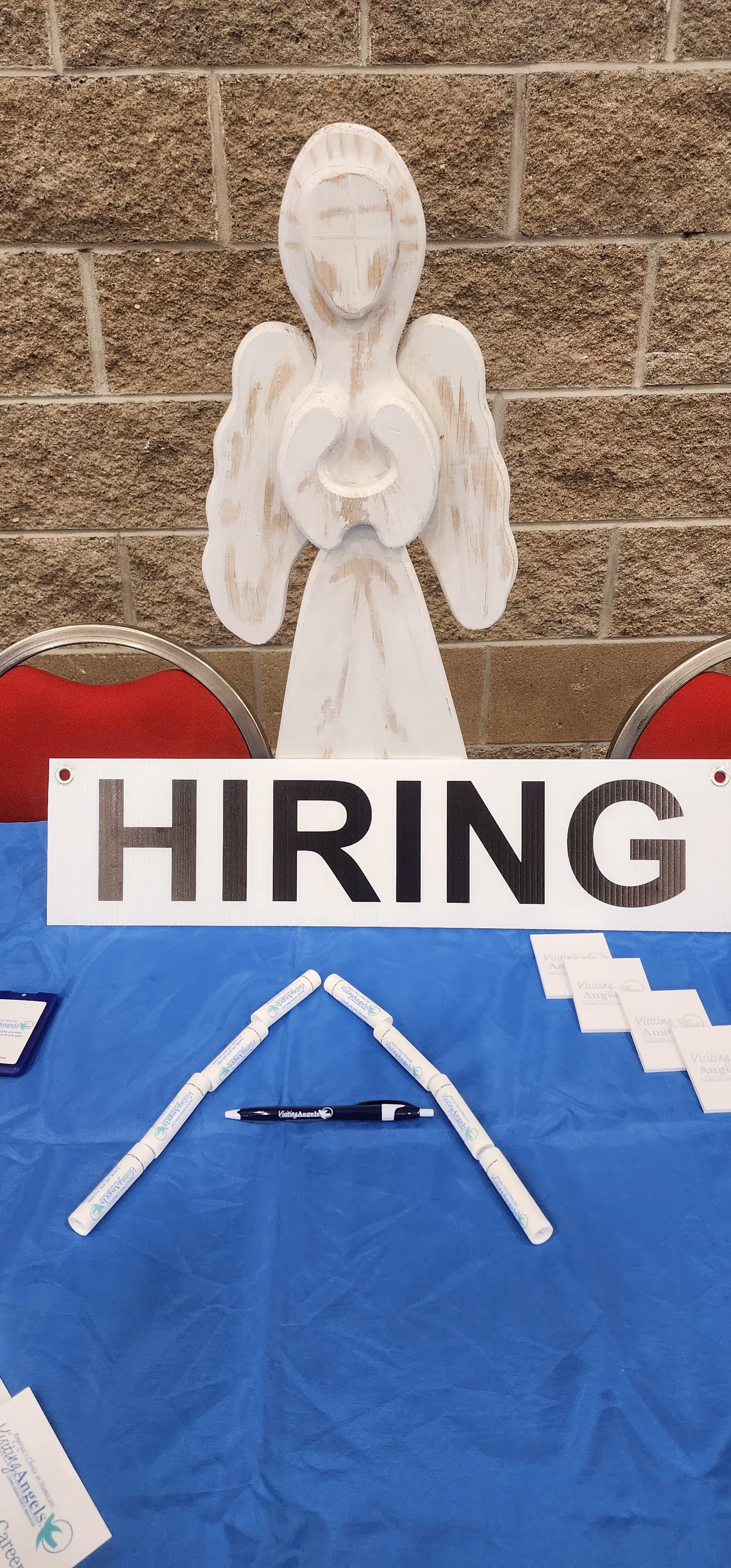 White angel statue stands behind a blue table with a large Hiring sign.