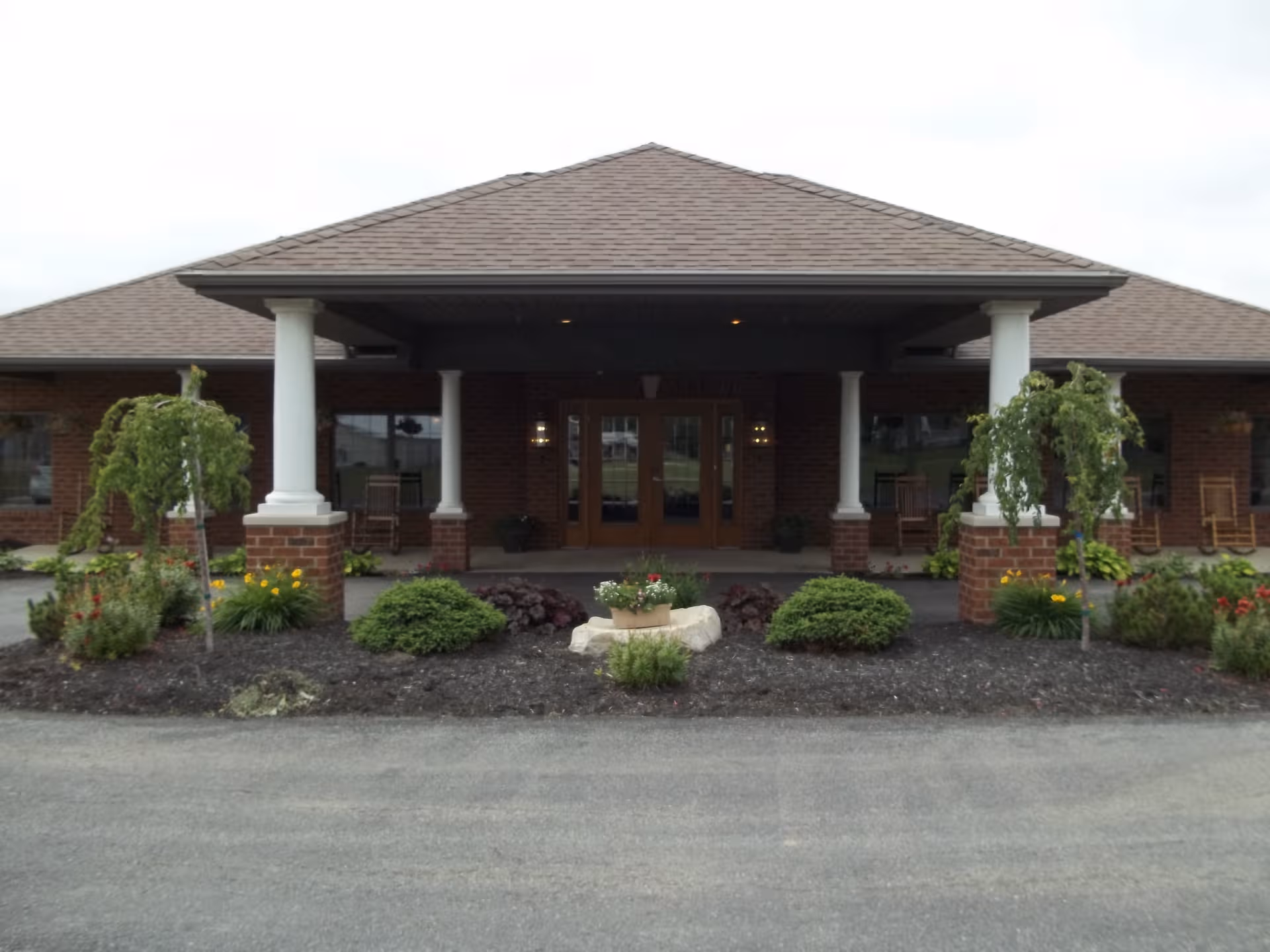 Brick entrance to an assisted living facility with columns and landscaped front yard.